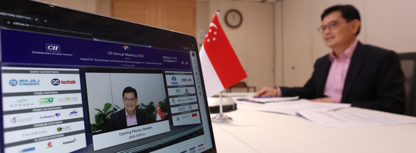 Laptop showing CII Annual Meeting, man on screen and in room with Singapore flag.