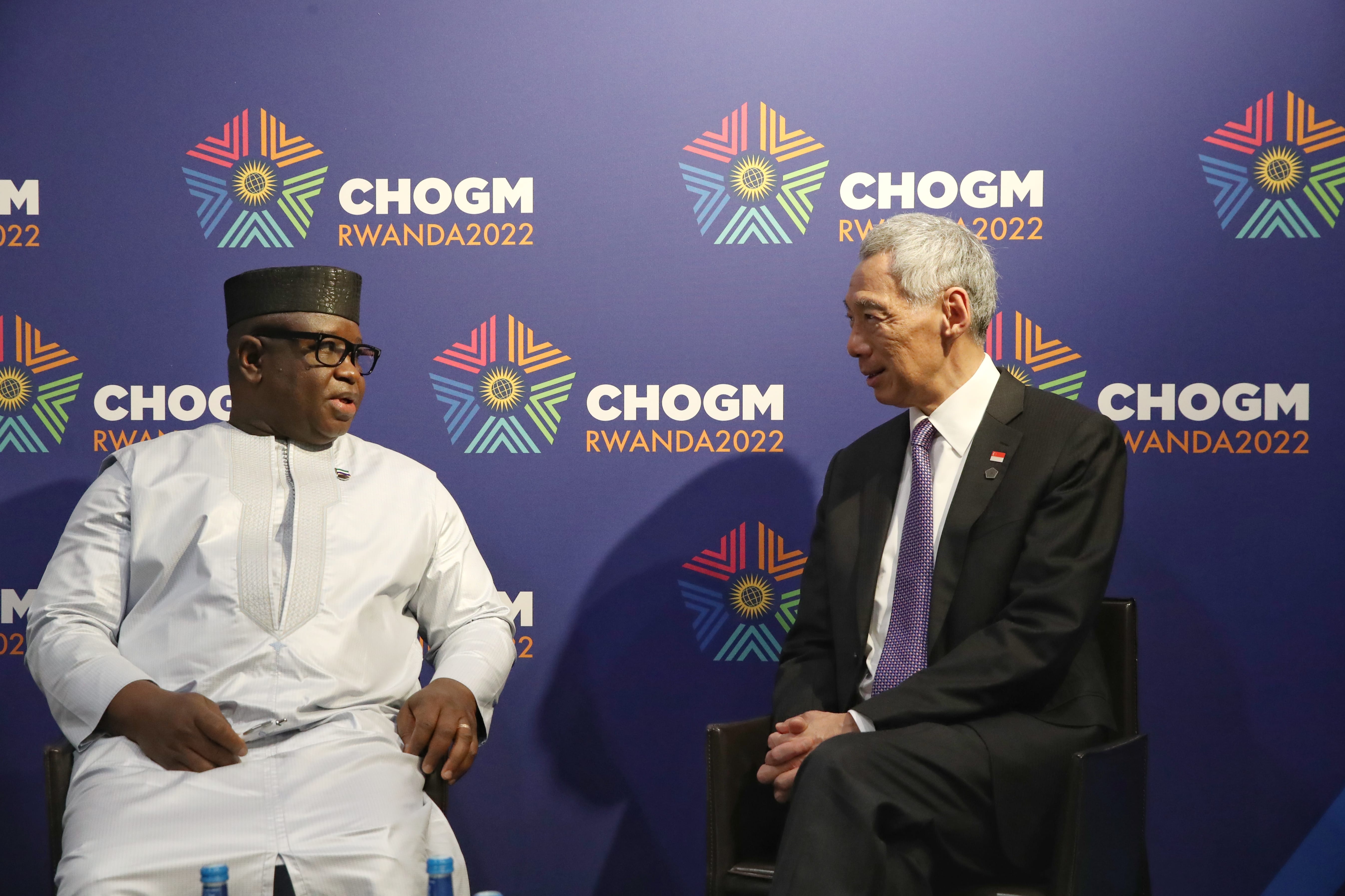 Two men seated, facing each other, against a "CHOGM RWANDA2022" branded blue backdrop.