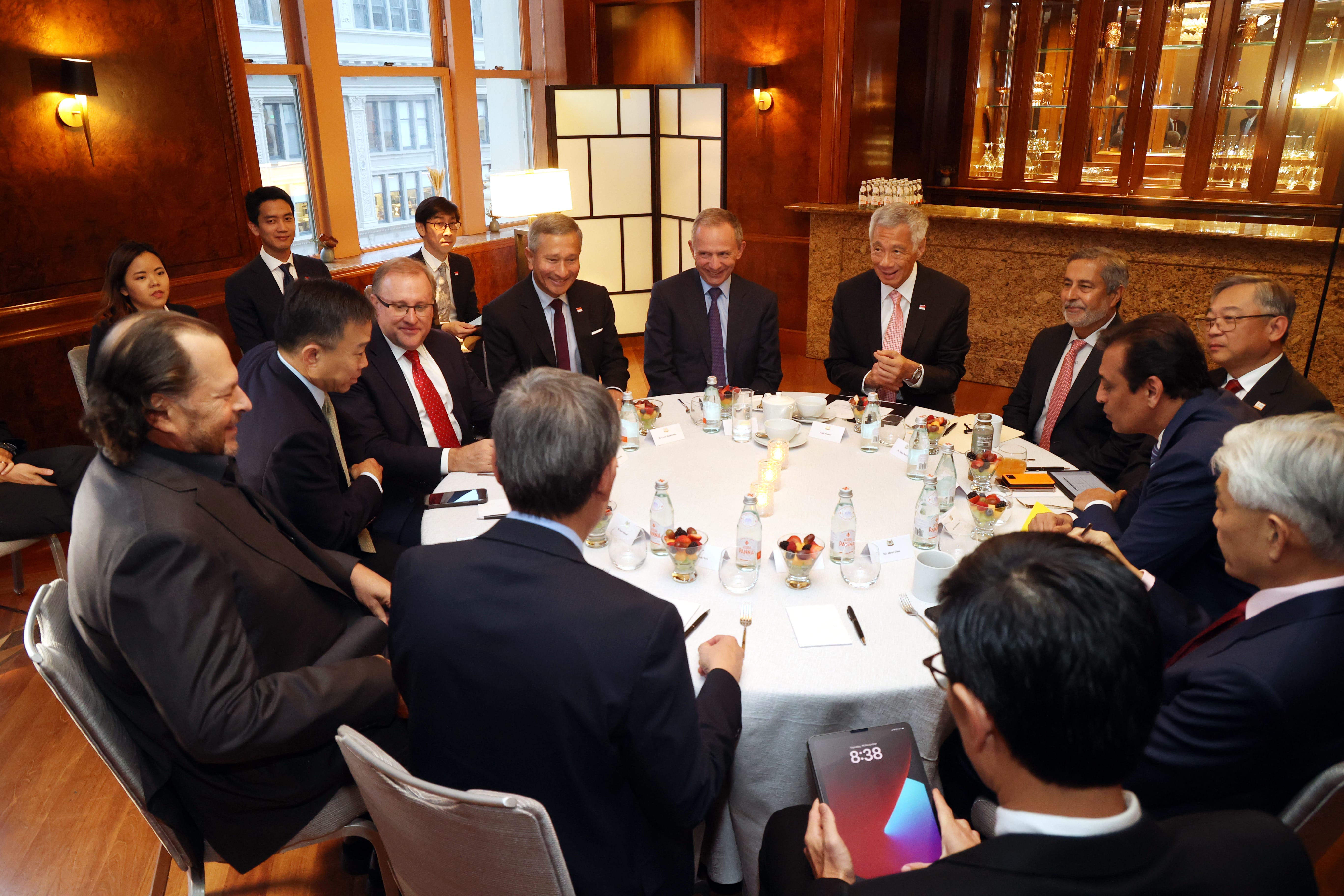 Group of people in suits sit around a table; Panna bottled water and fruit bowls are present.