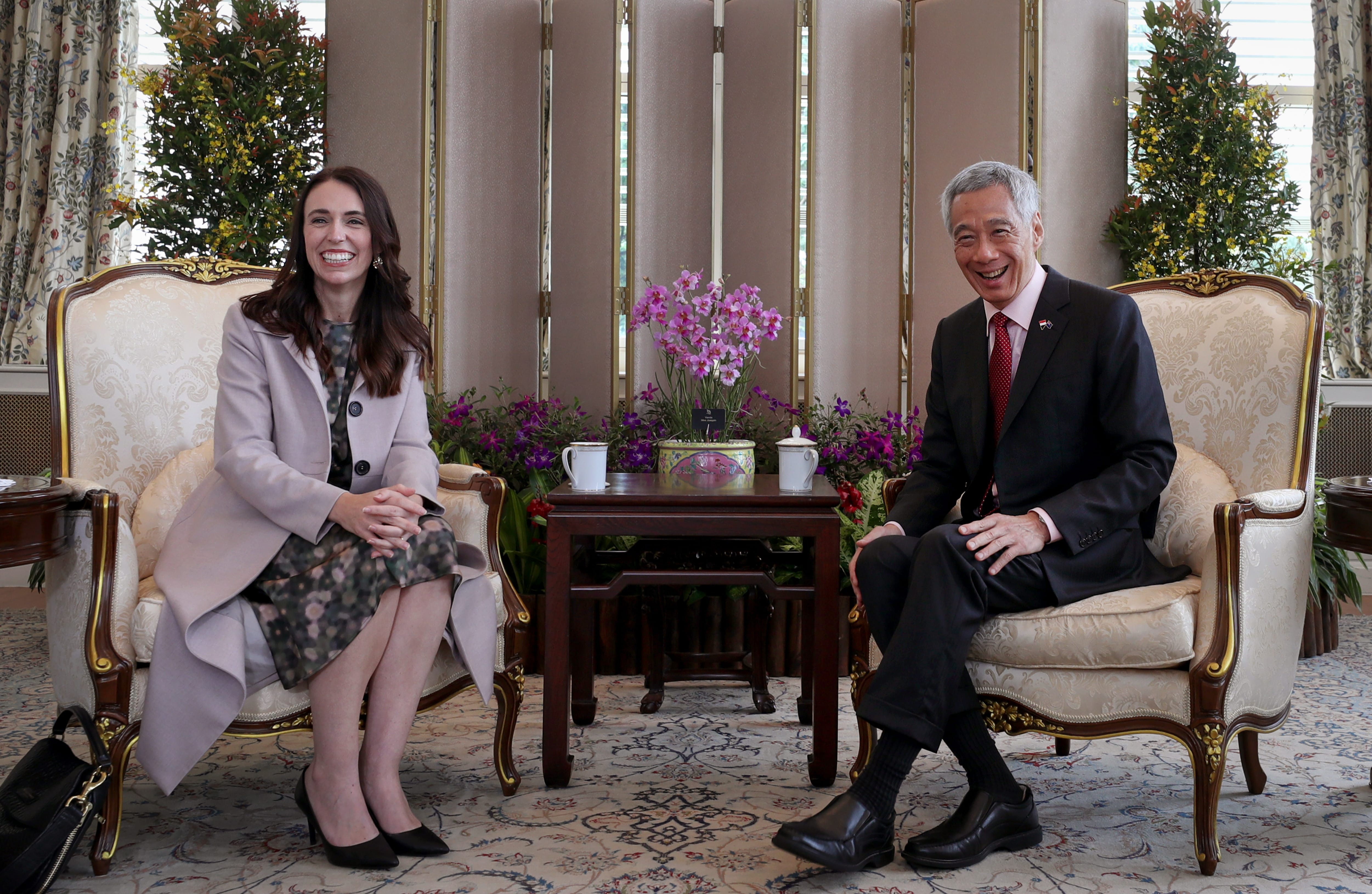 Jacinda Ardern and Lee Hsien Loong seated in ornate chairs in formal setting.
