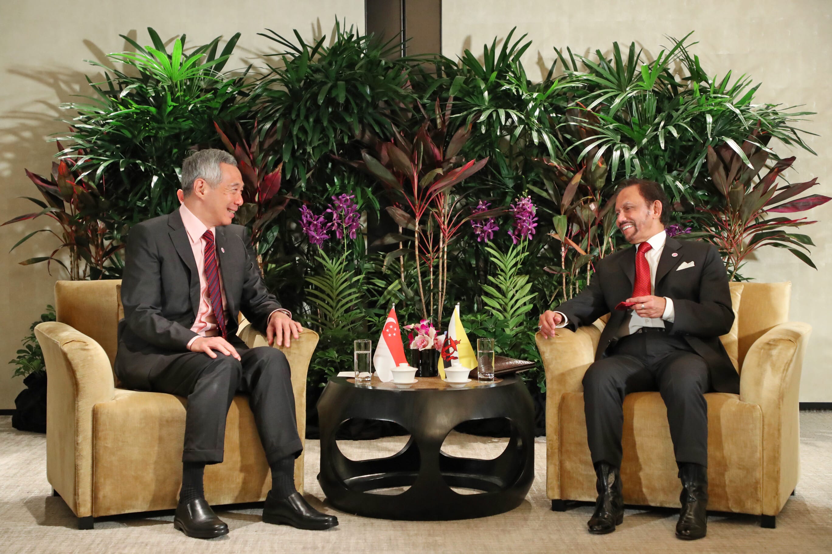 Lee Hsien Loong & Sultan of Brunei sit in golden chairs facing each other with flags on a table between them.
