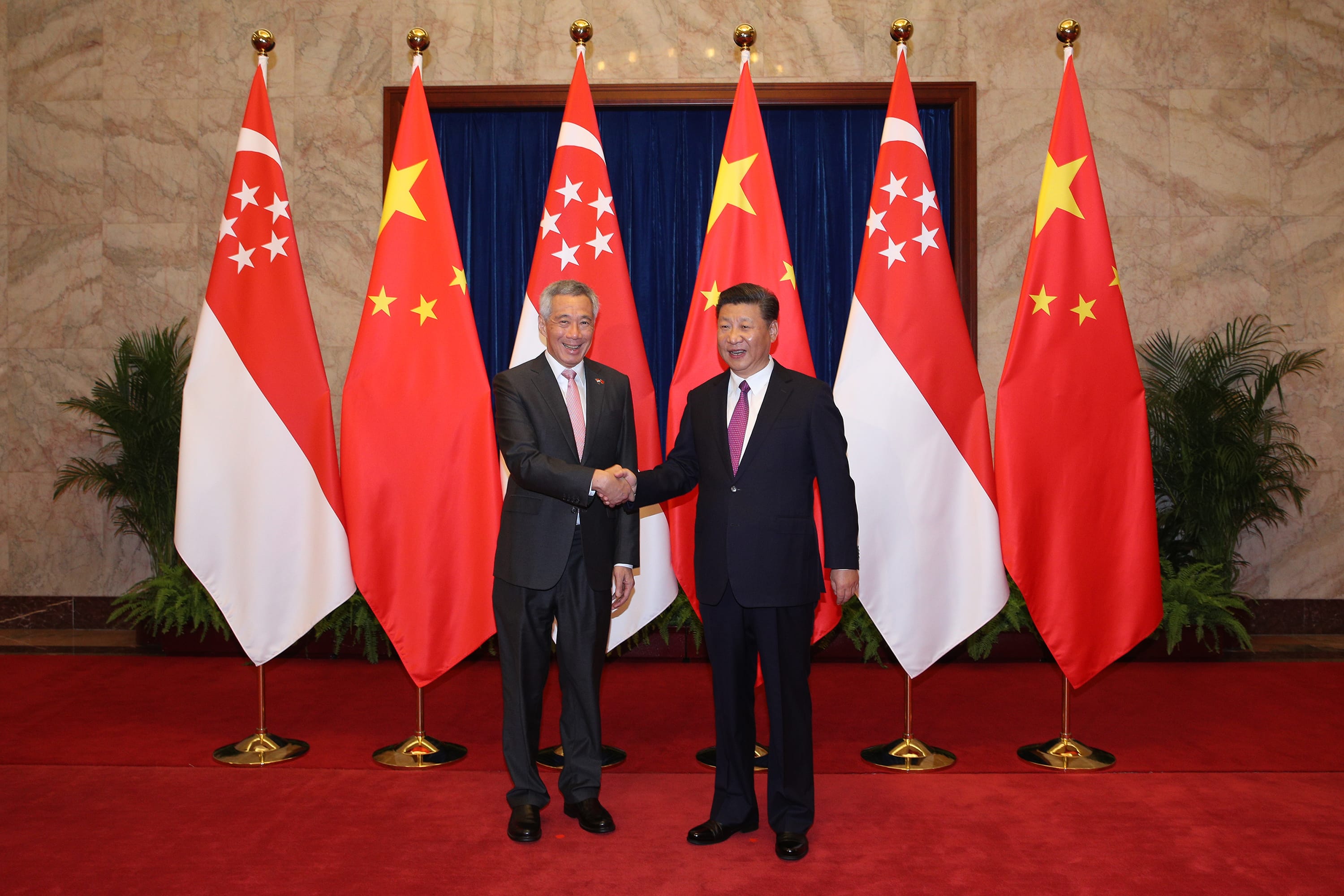 Lee Hsien Loong and Xi Jinping shake hands before Singaporean and Chinese flags.