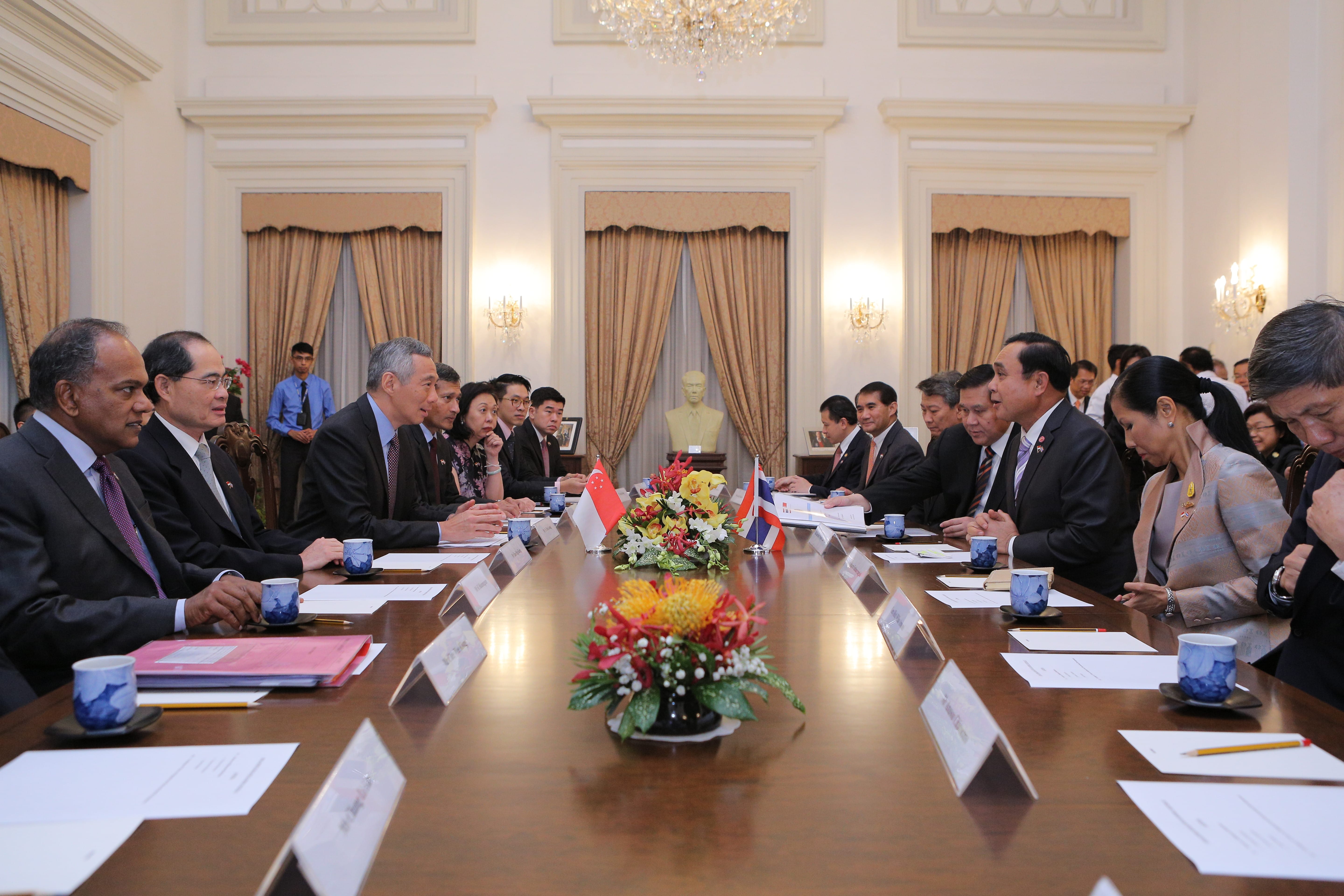 People in suits seated at a long conference table with flower arrangements and country flags.