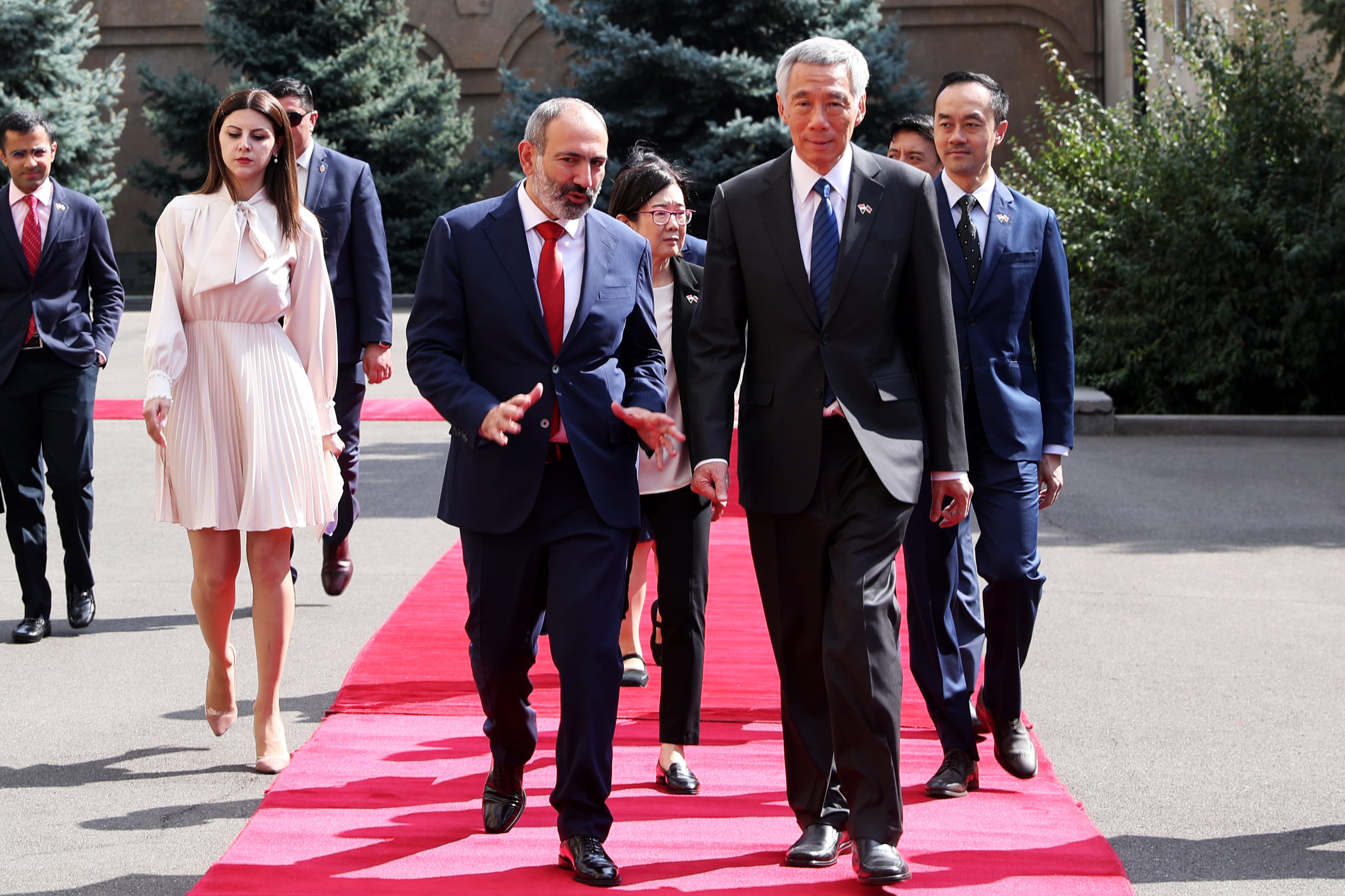 Lee Hsien Loong walks a red carpet, followed by Nikol Pashinyan and others in suits.