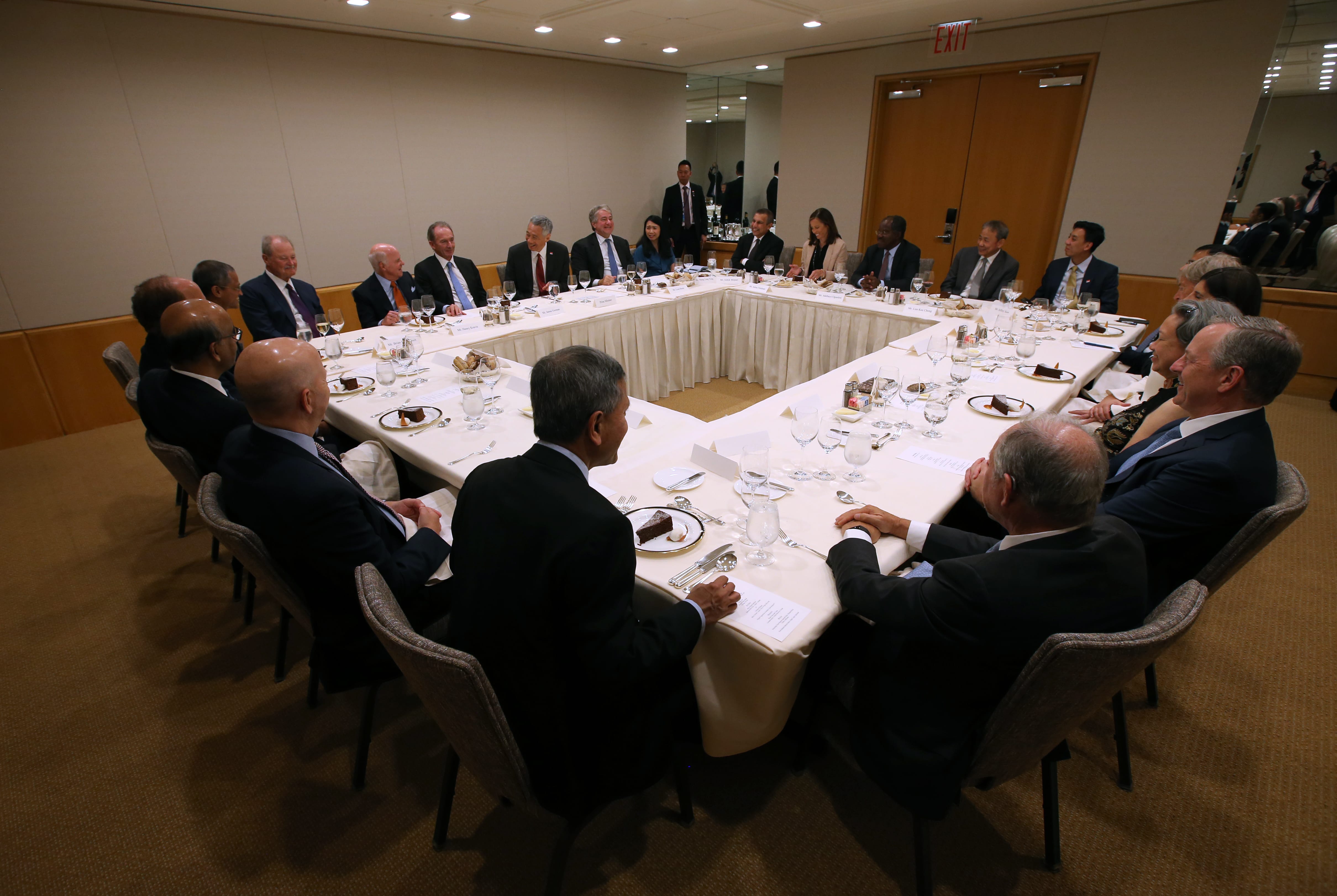 Group seated at a square table set with dinnerware in a neutral room.