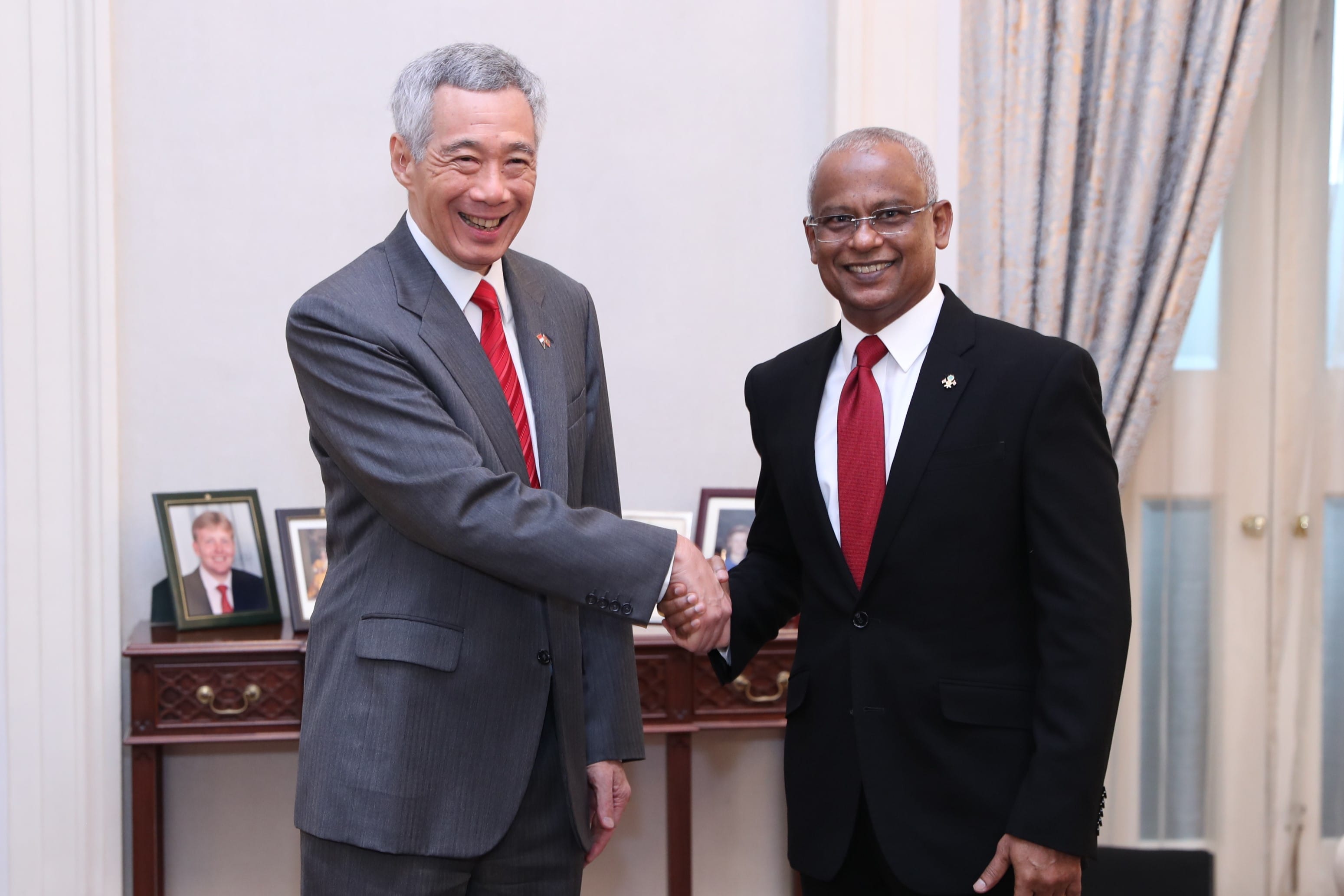 Two men in suits, Lee Hsien Loong and Abdulla Shahid, shake hands in a room with framed photos.