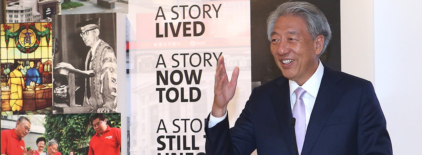 Man in suit waves by "A Story Lived" wall collage of OCBC Wing Hang Bank history.