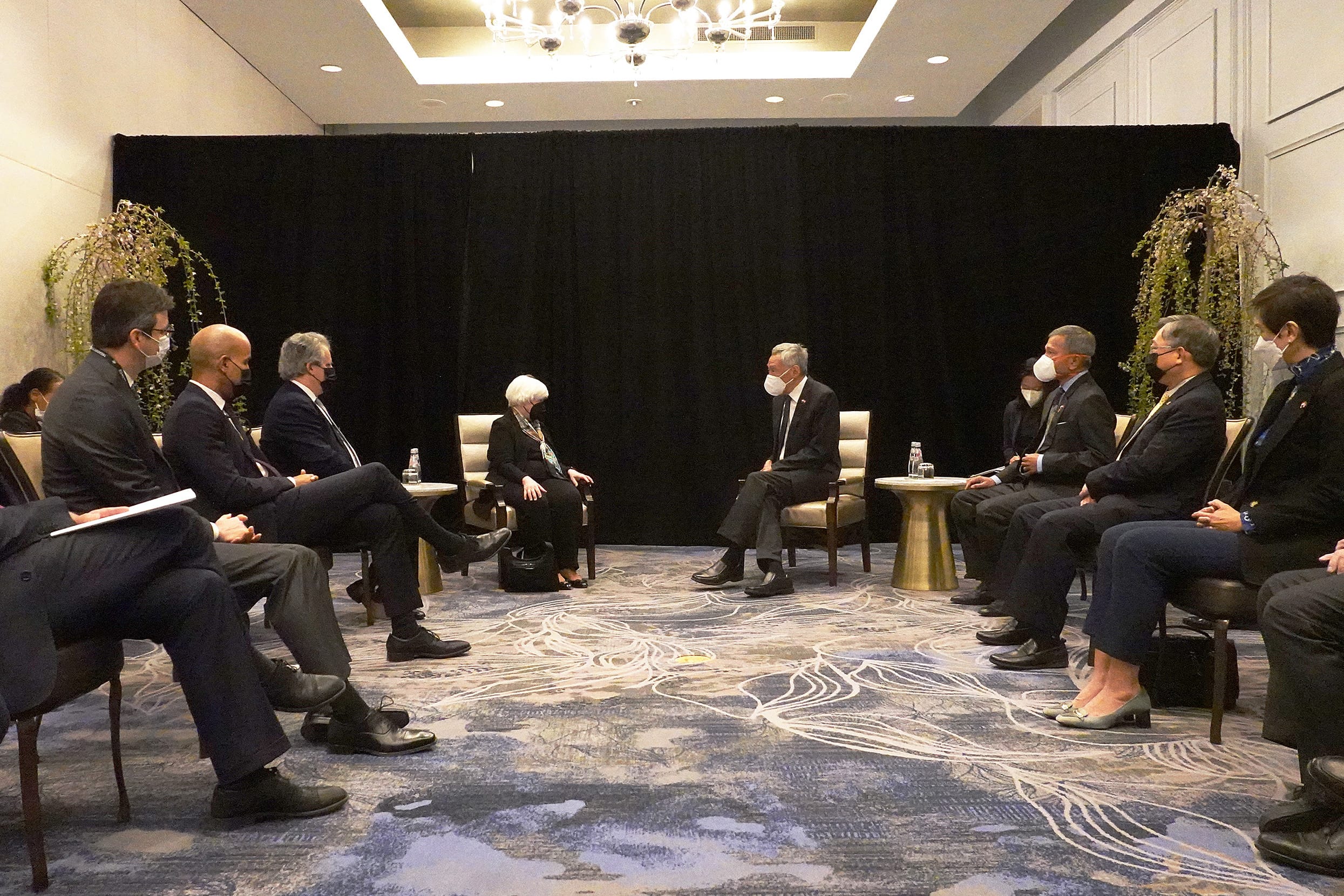 People in suits sit in chairs, facing each other, wearing face masks in a meeting room. Janet Yellen is present.