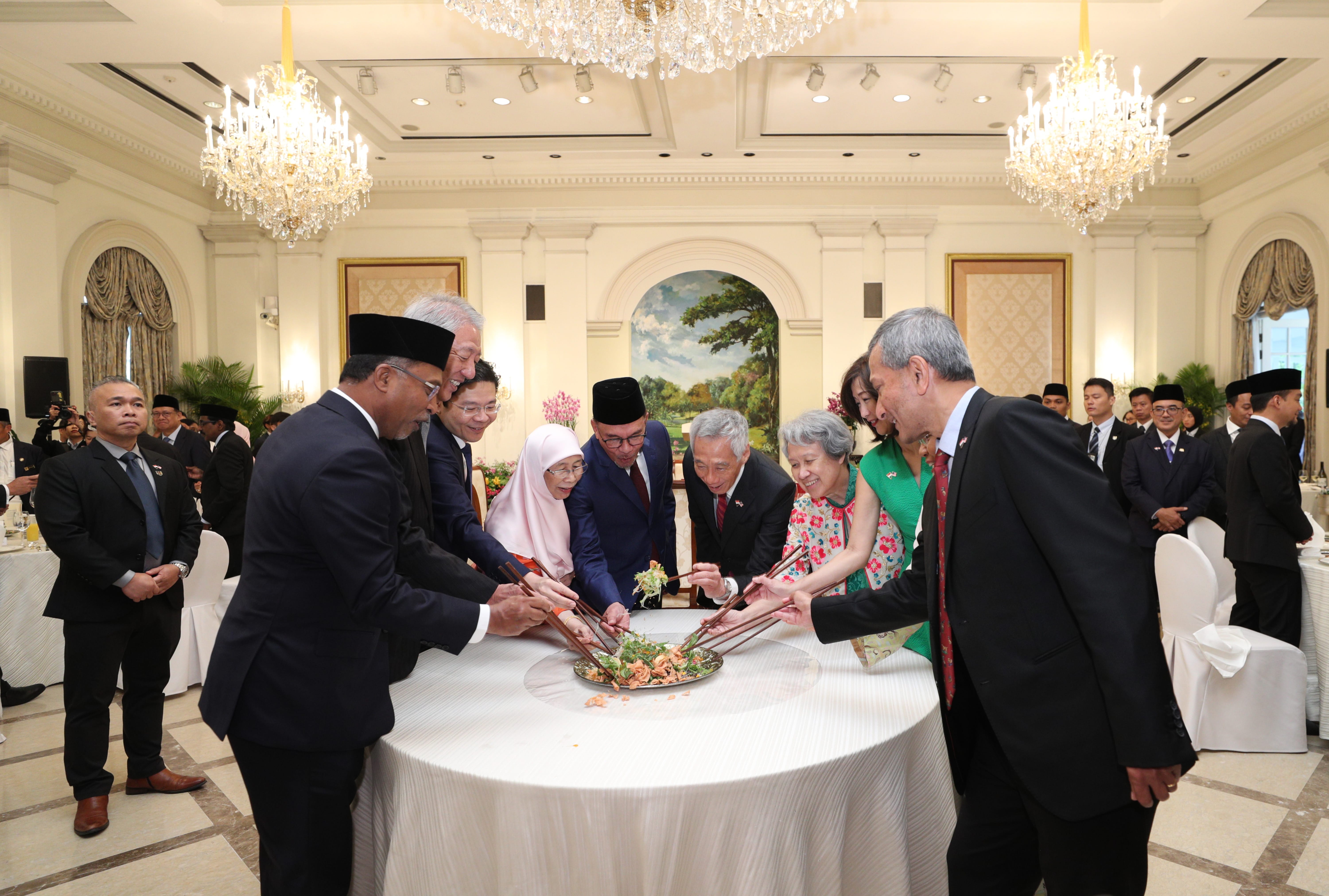 Group of people tossing salad with chopsticks around a table in an ornate room.