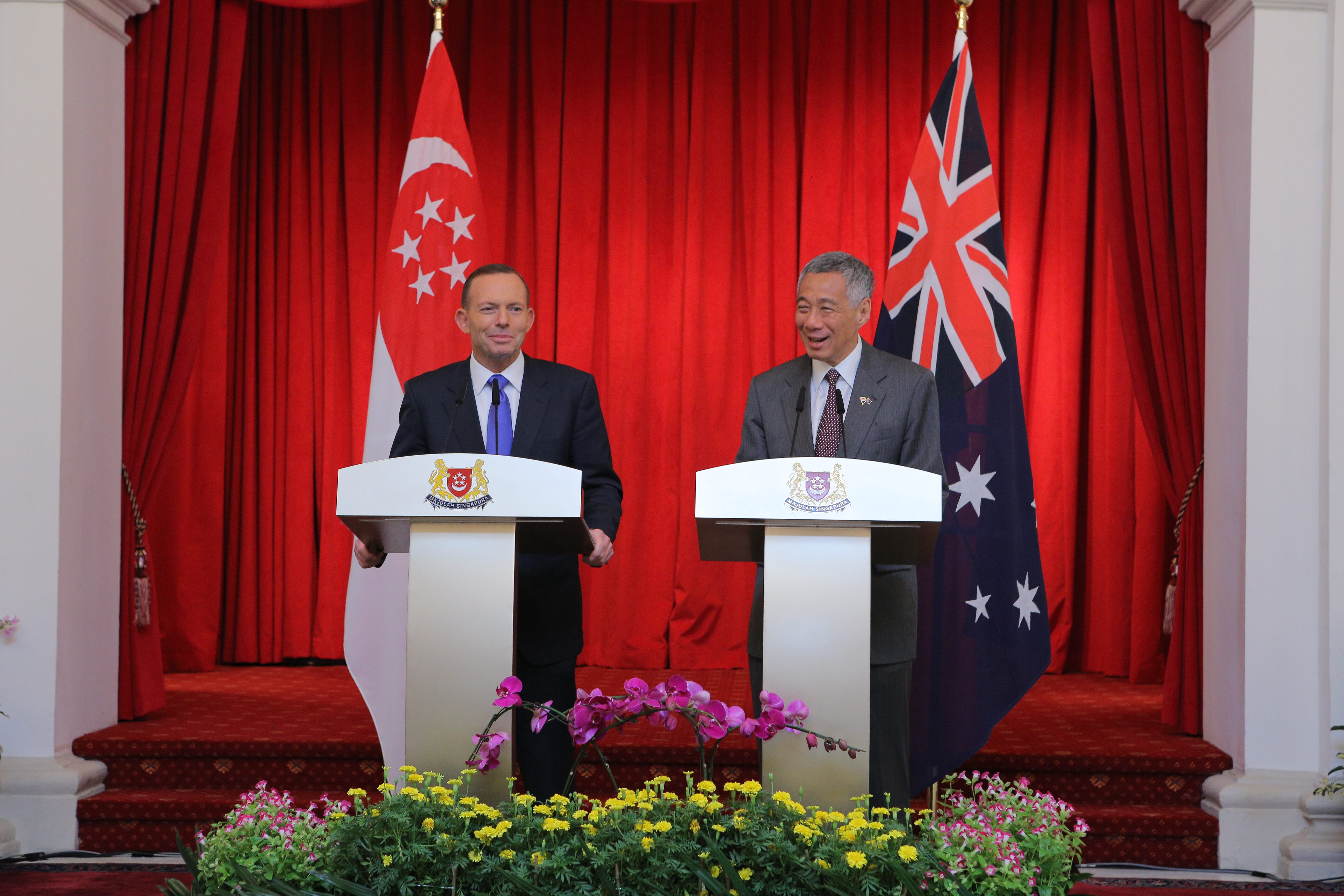 Tony Abbott and Lee Hsien Loong at podiums with Singaporean and Australian flags behind them.