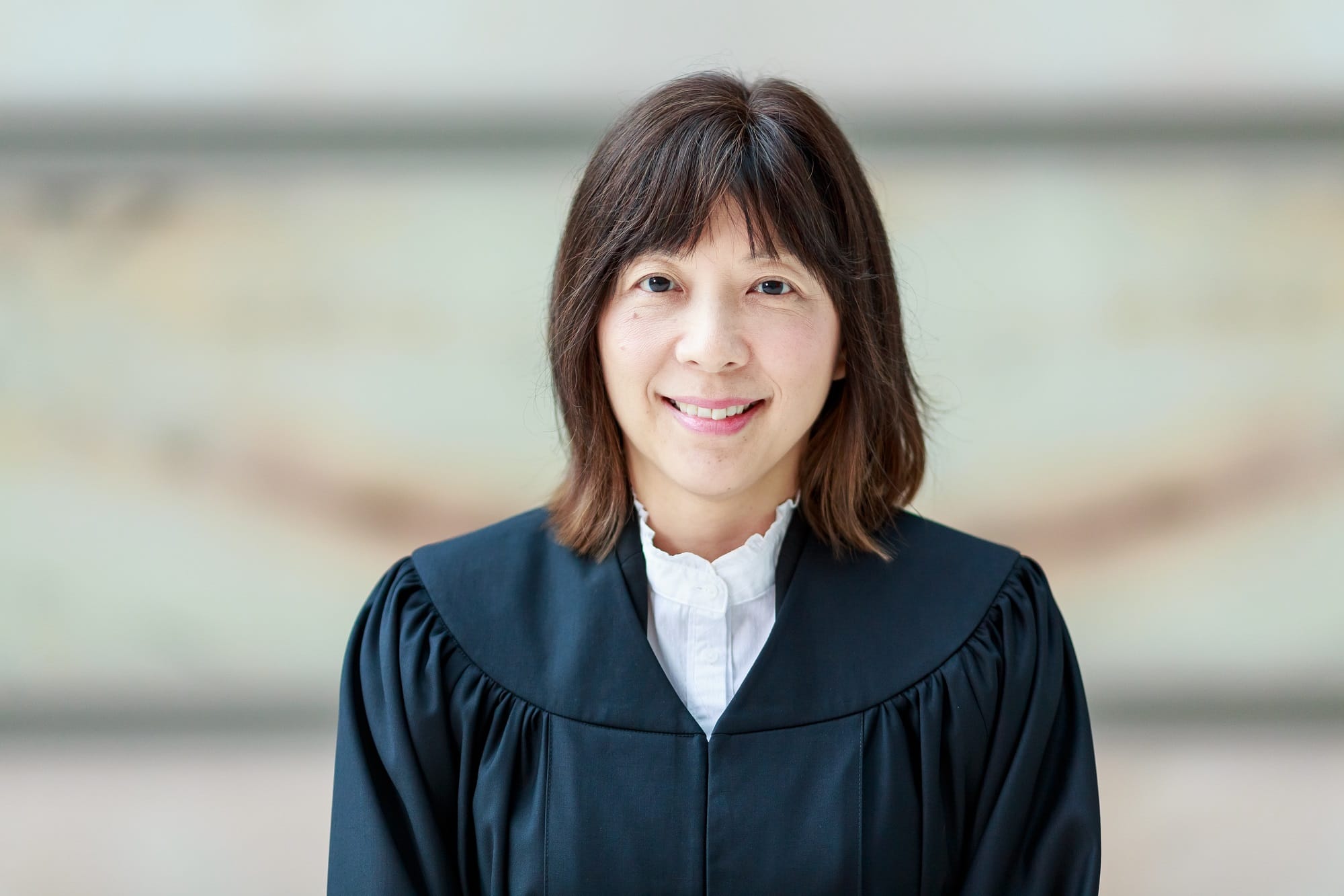 Person with shoulder-length hair in a black academic gown smiles at the camera.
