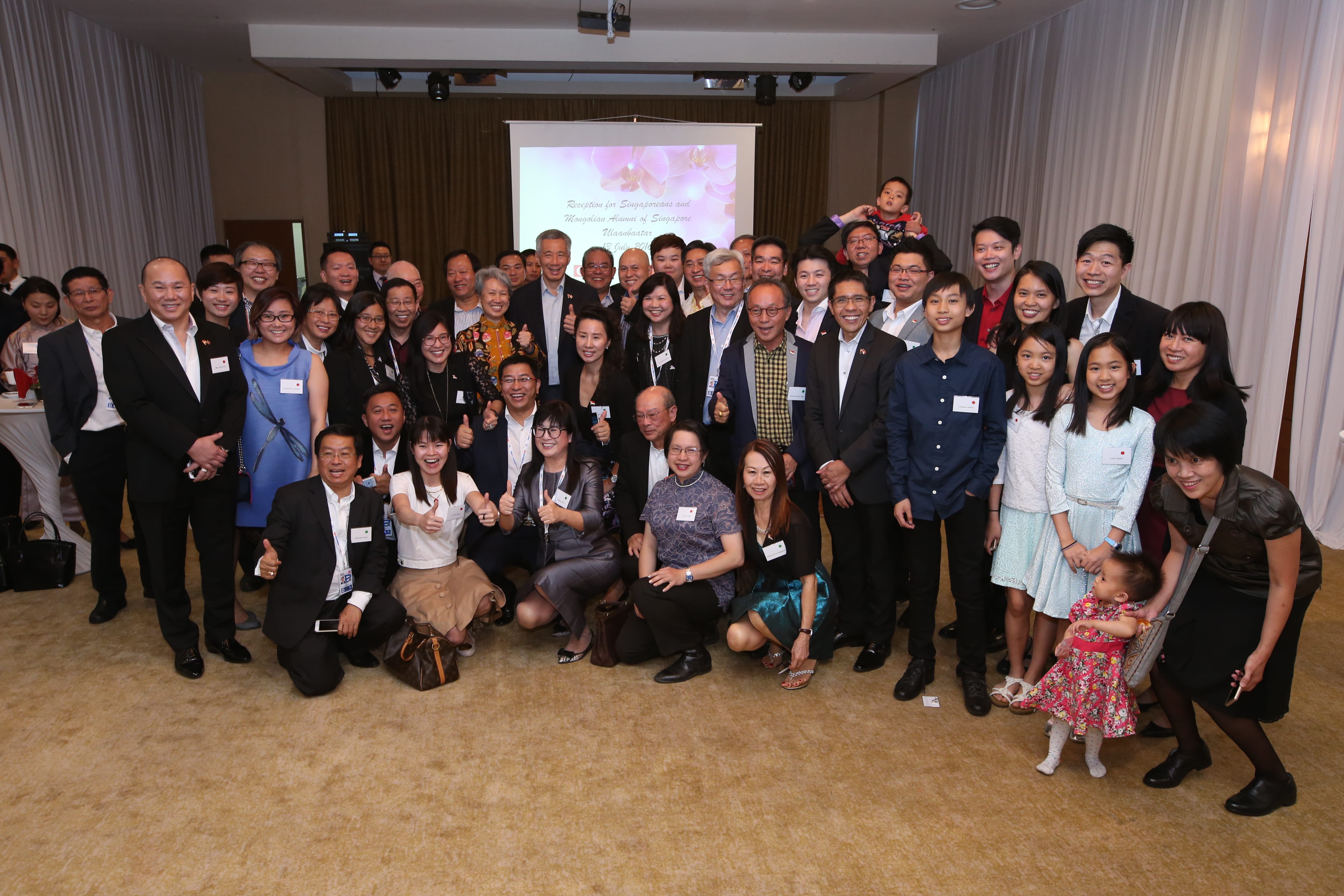 Large group of diverse adults and children posing for a photo at an event, some giving thumbs up.