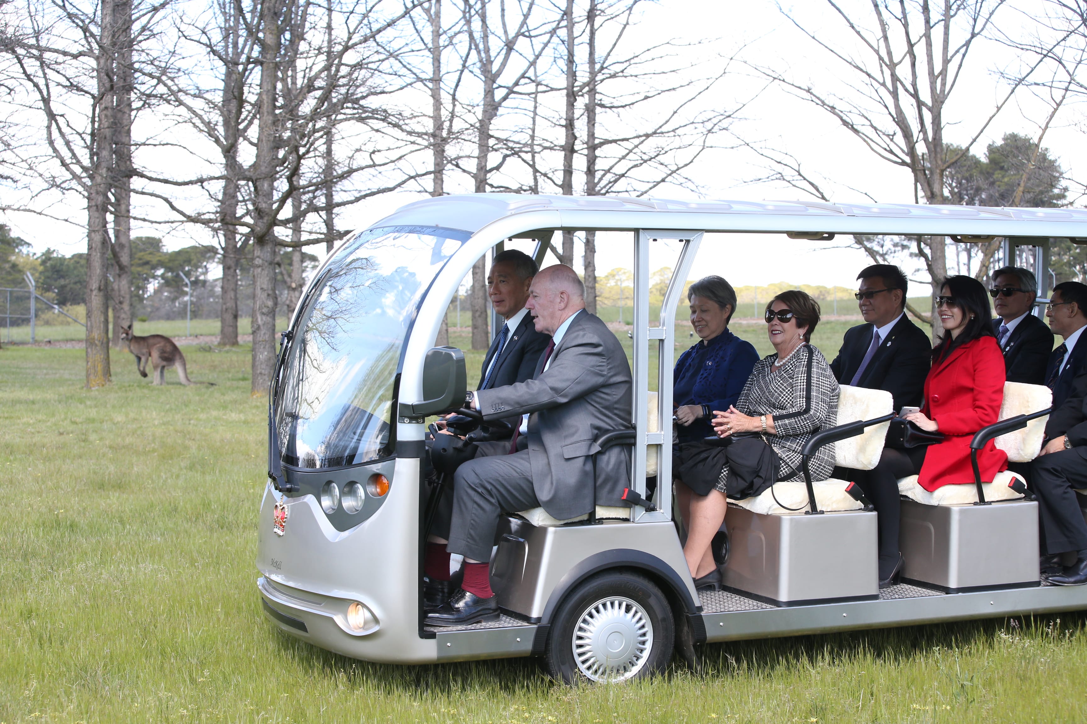 People in a McKell buggy driving on grass, kangaroo visible in the background.