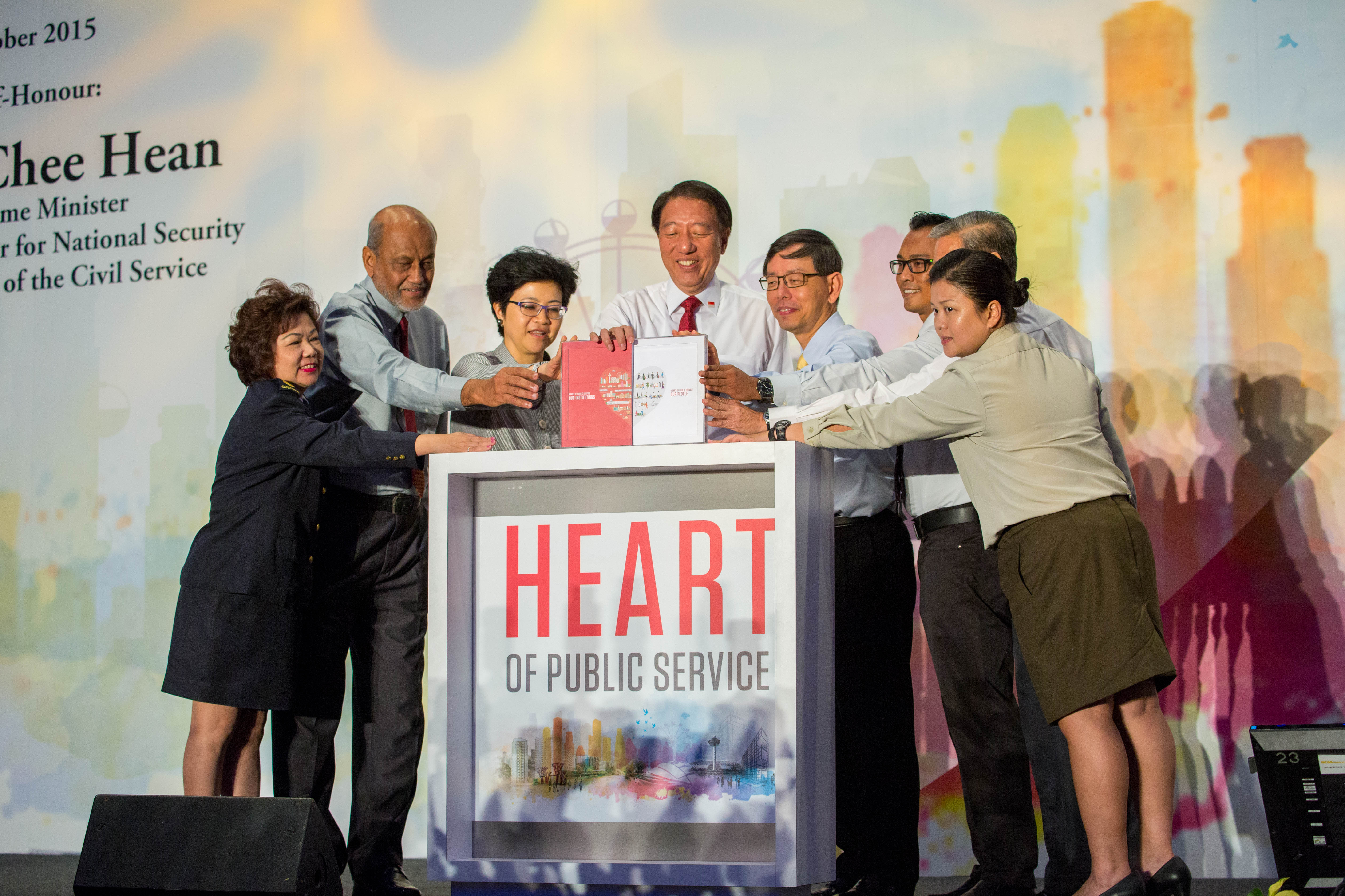 Group of people present books with "HEART OF PUBLIC SERVICE" on a stand at an event.