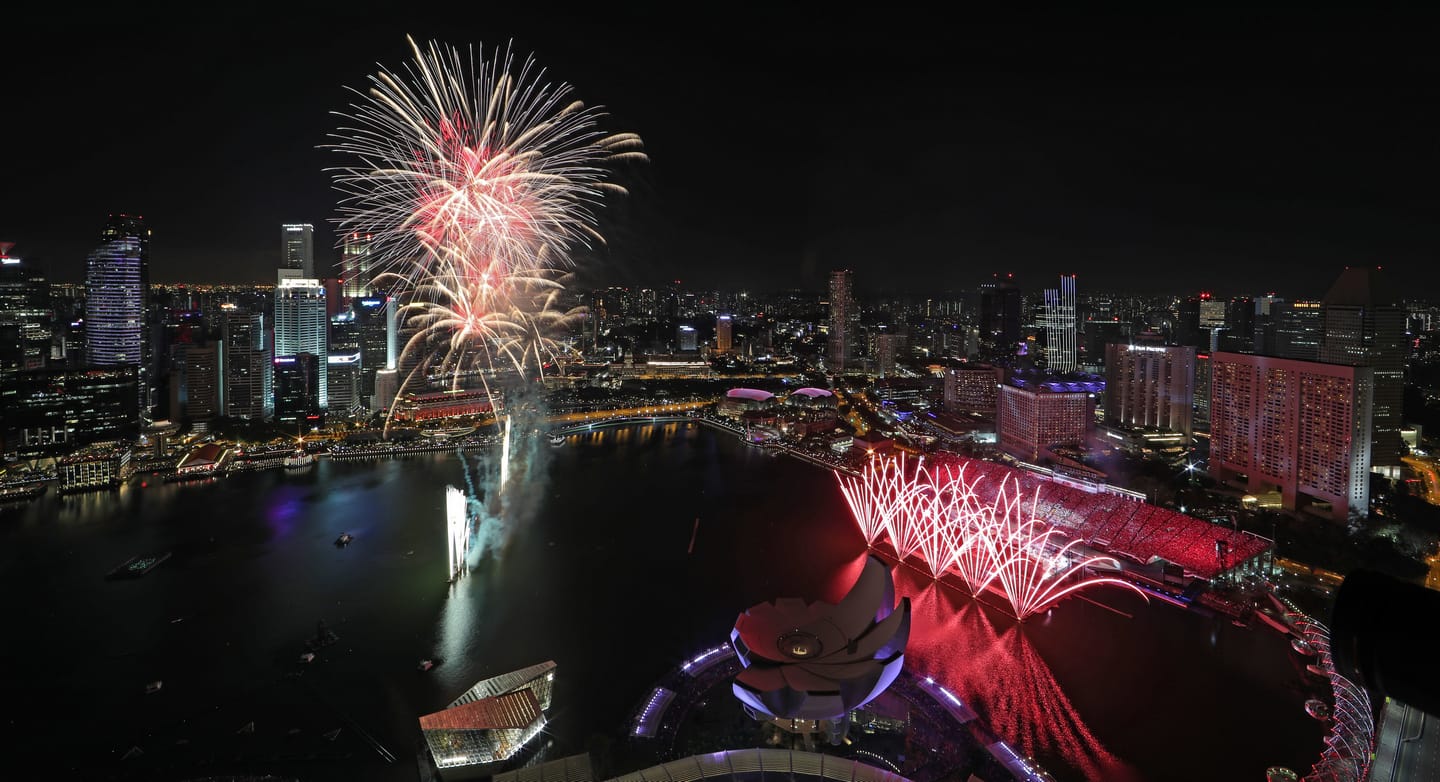 City skyline at night with fireworks over water, buildings lit up.