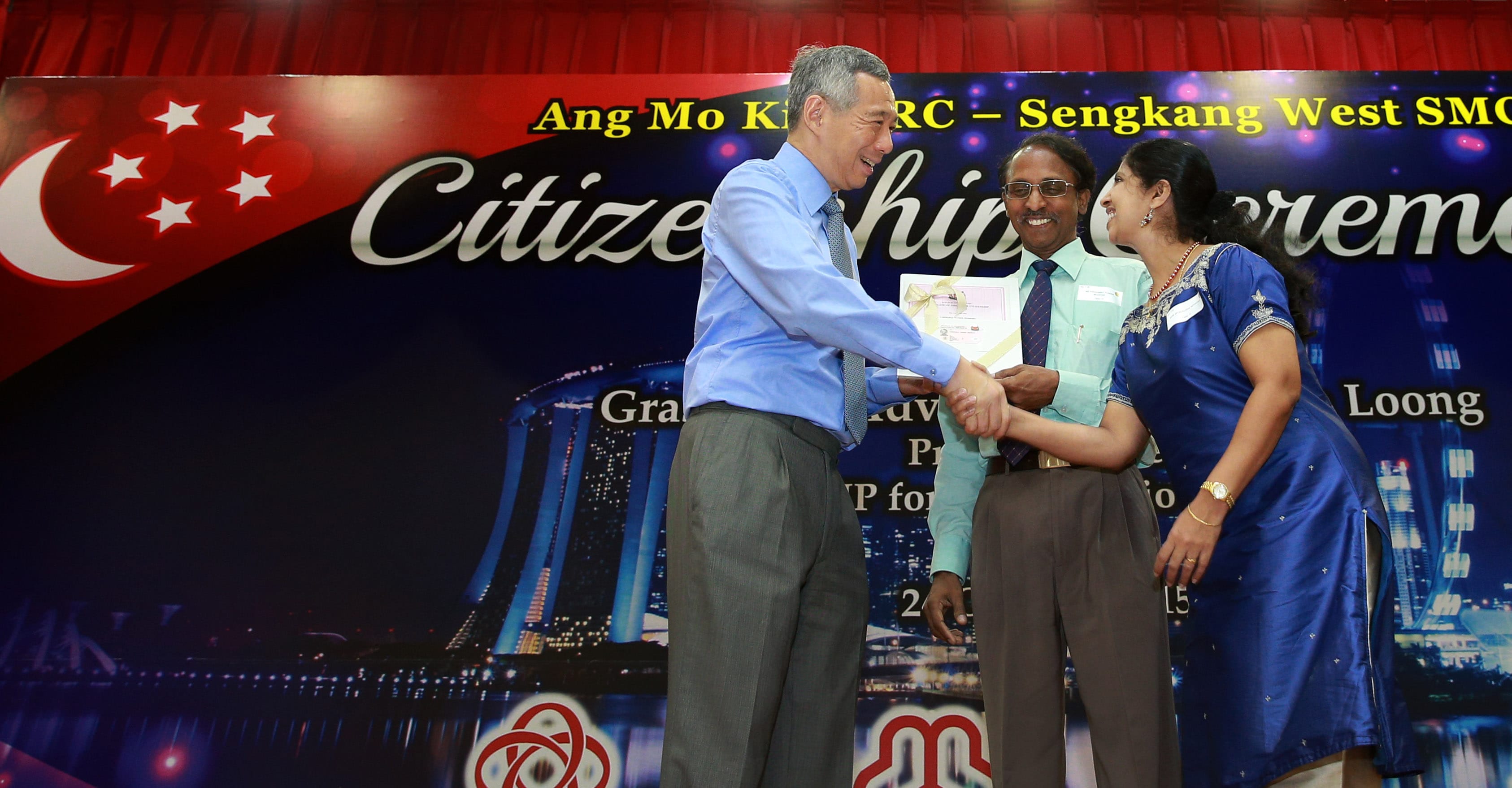 Lee Hsien Loong presents certificate and shakes hands with couple at event.
