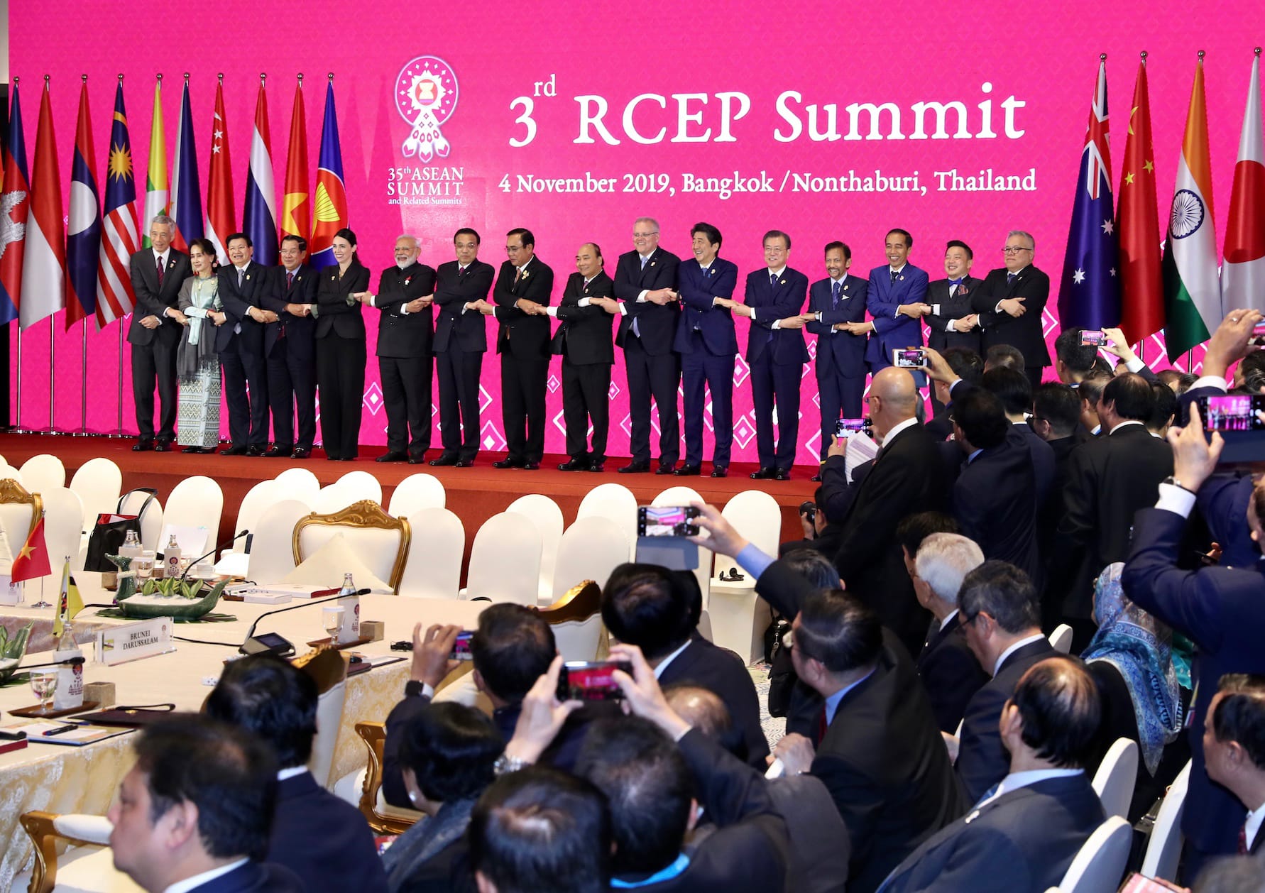 World leaders holding hands on stage at 3rd RCEP Summit with flags and attendees.