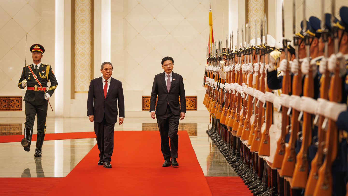 Two men in suits walk a red carpet past a guard of honor with rifles.