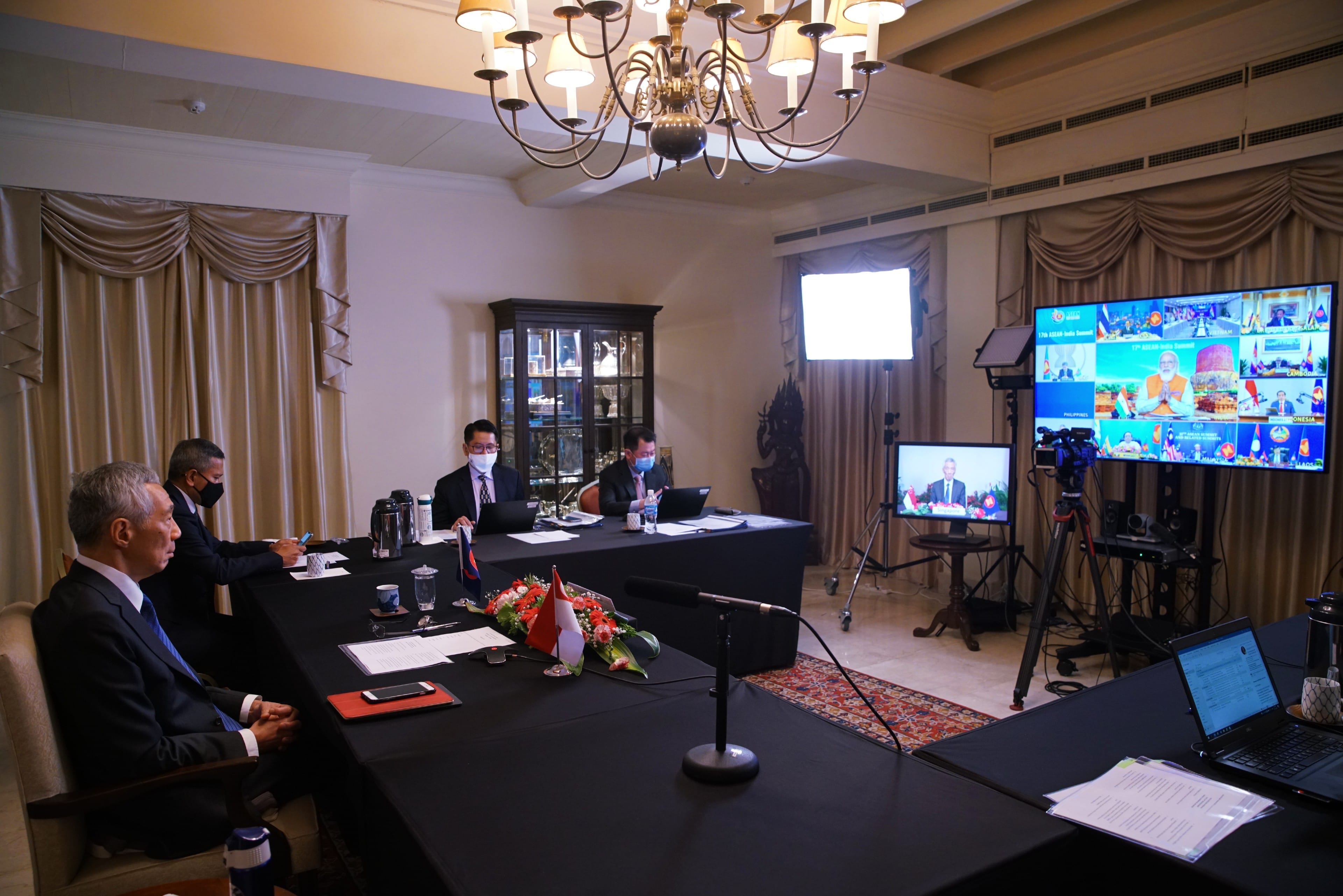 People in suits at a long table, plus video screens and camera equipment.