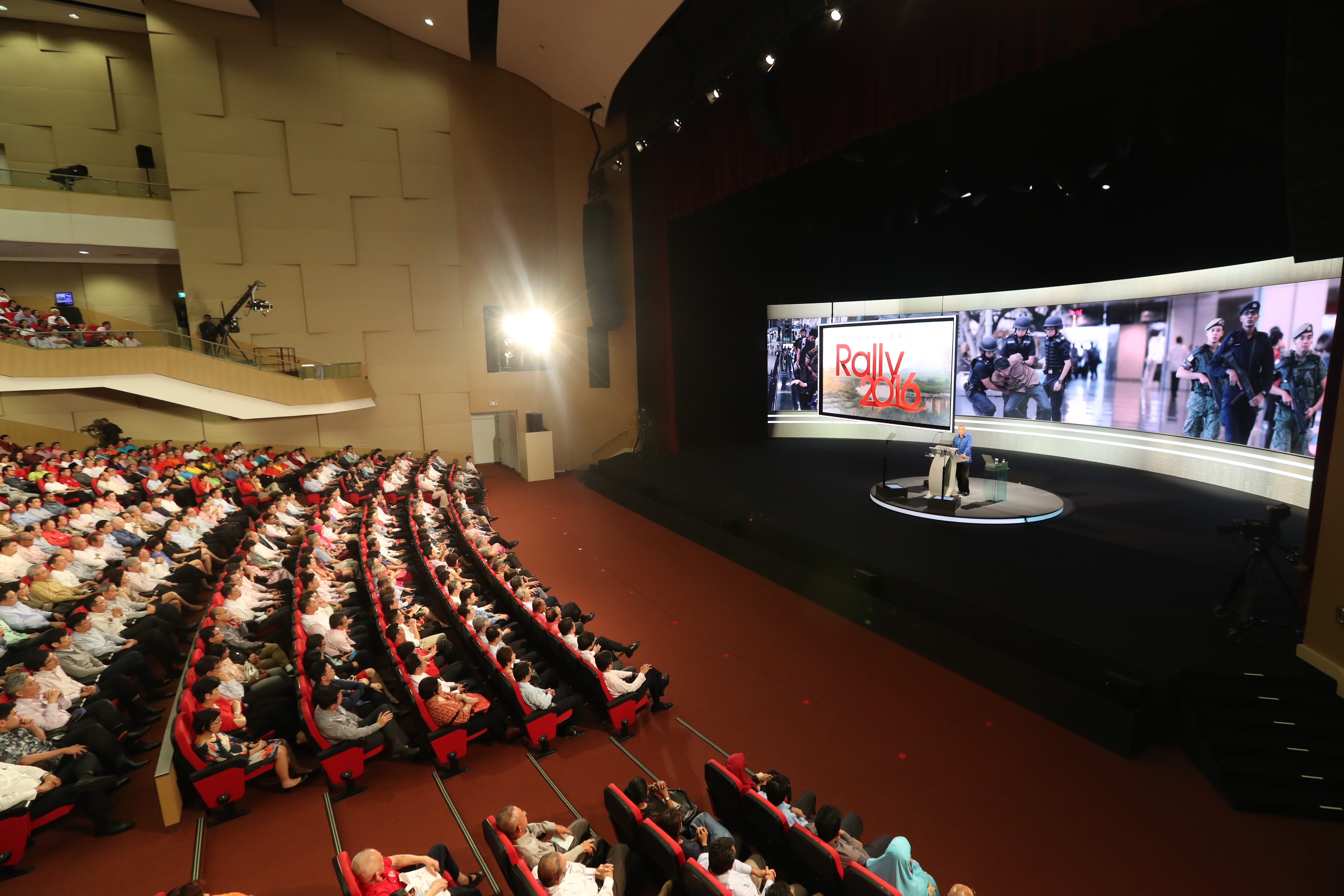 Auditorium with audience watching a "Rally 2016" presentation on a large screen.