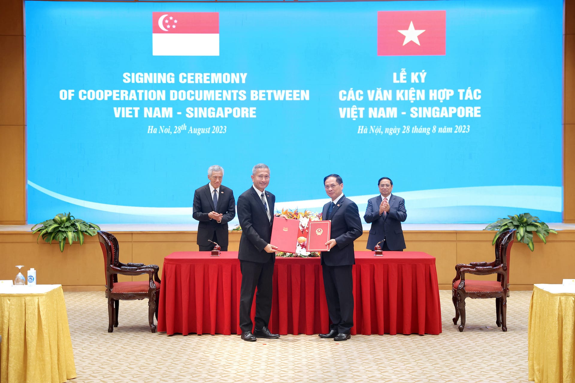 Two men in suits exchange documents, behind them flags of Singapore and Vietnam.