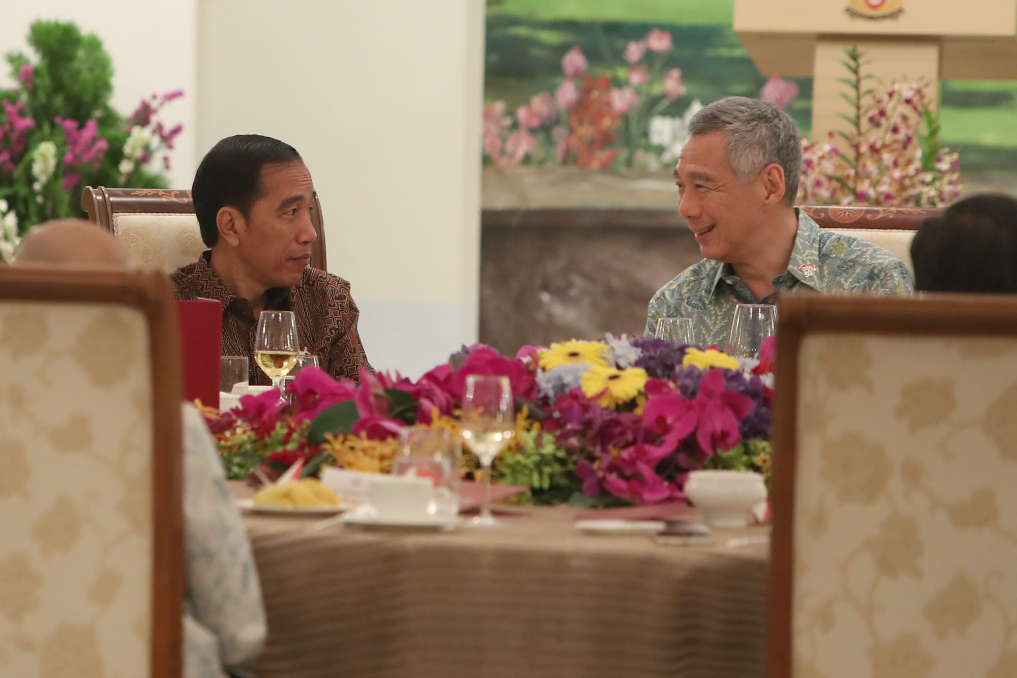 Joko Widodo and Lee Hsien Loong at a table with flowers and drinks.