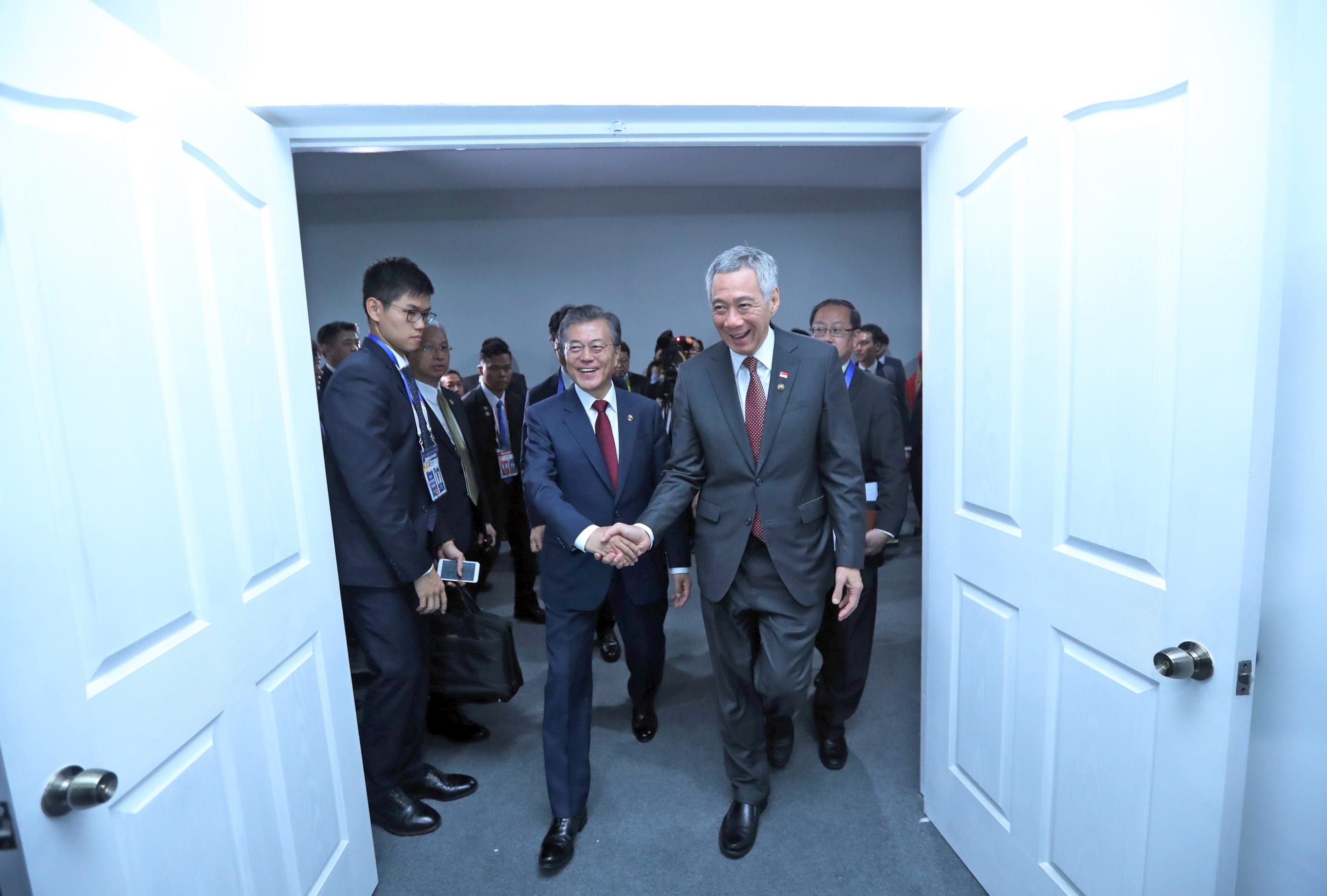 Lee Hsien Loong shakes hands with Moon Jae-in walking through a doorway, followed by others.