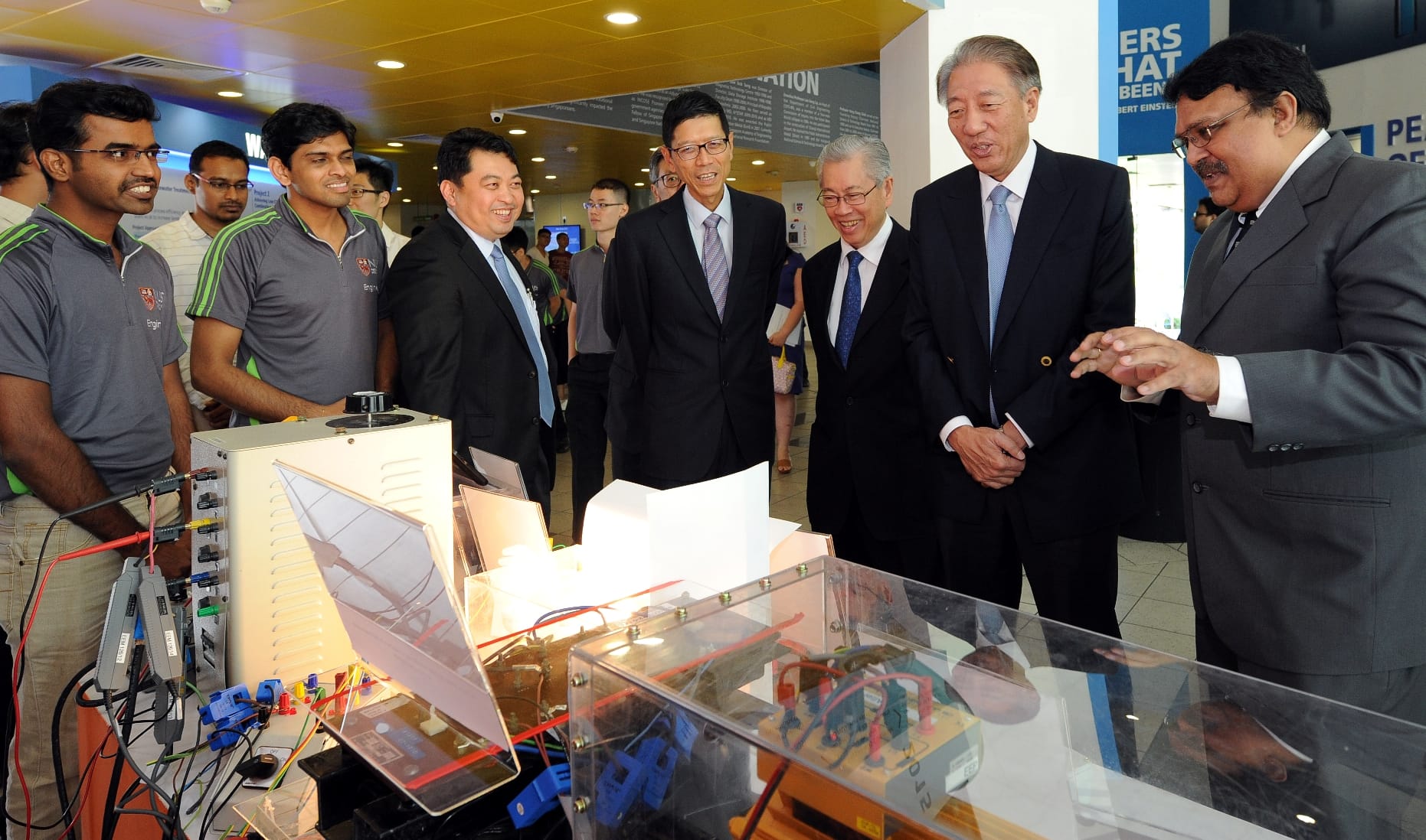 Group of men in suits and students examining a solar power science project.