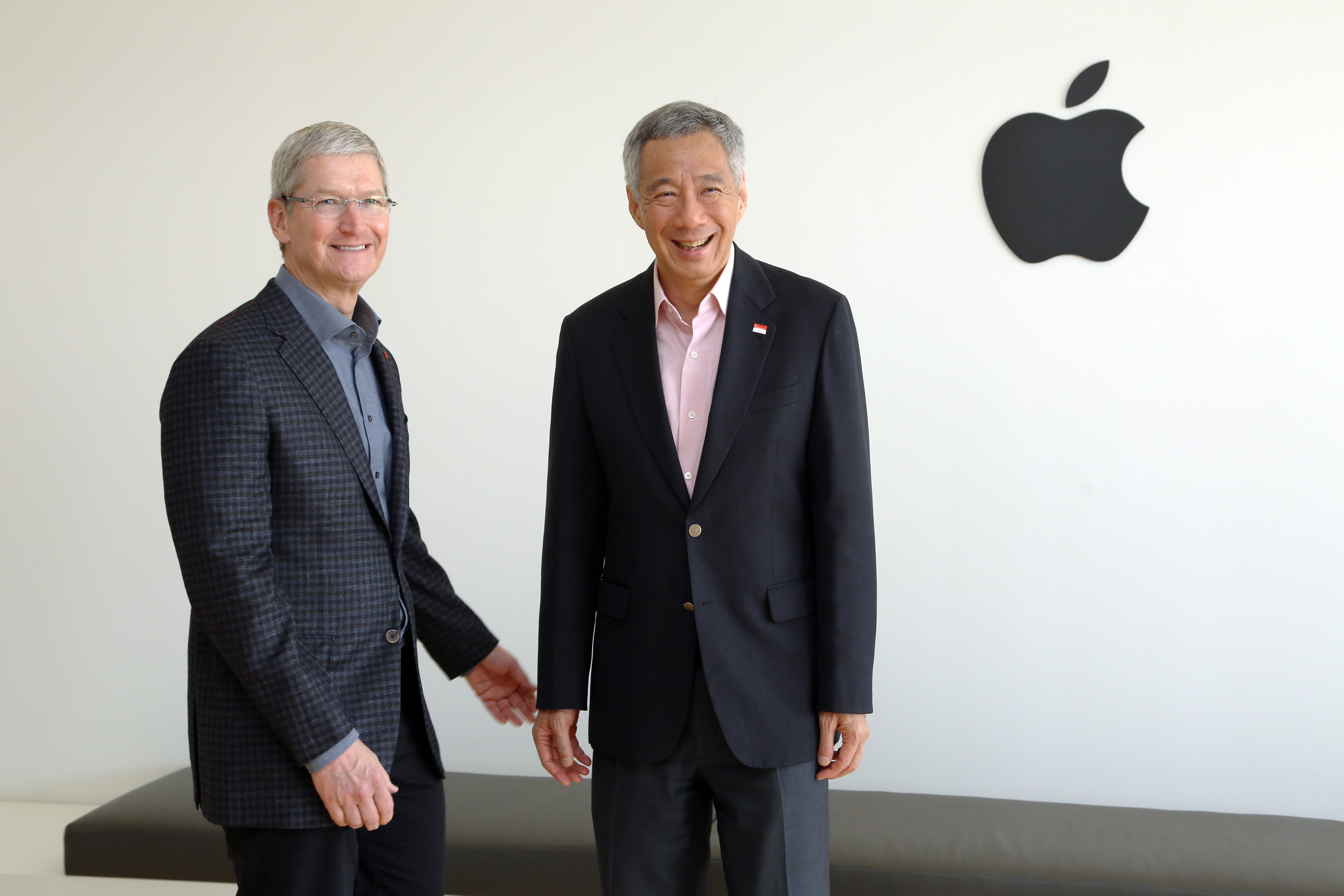 Tim Cook and Lee Hsien Loong stand smiling before a white wall with a black Apple logo.