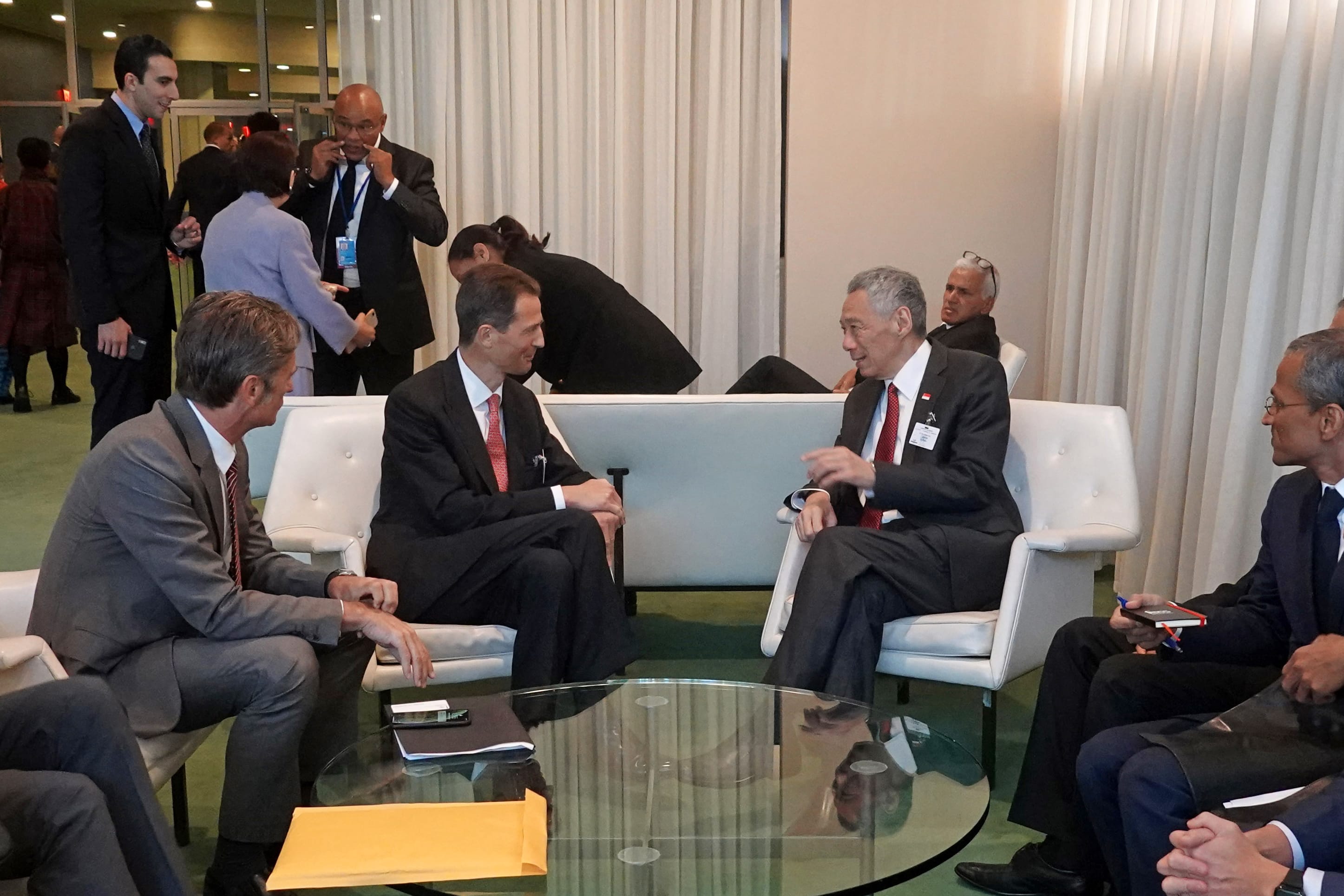 Lee Hsien Loong in suit sits, gesturing while speaking to another man also in a suit, in a meeting space.