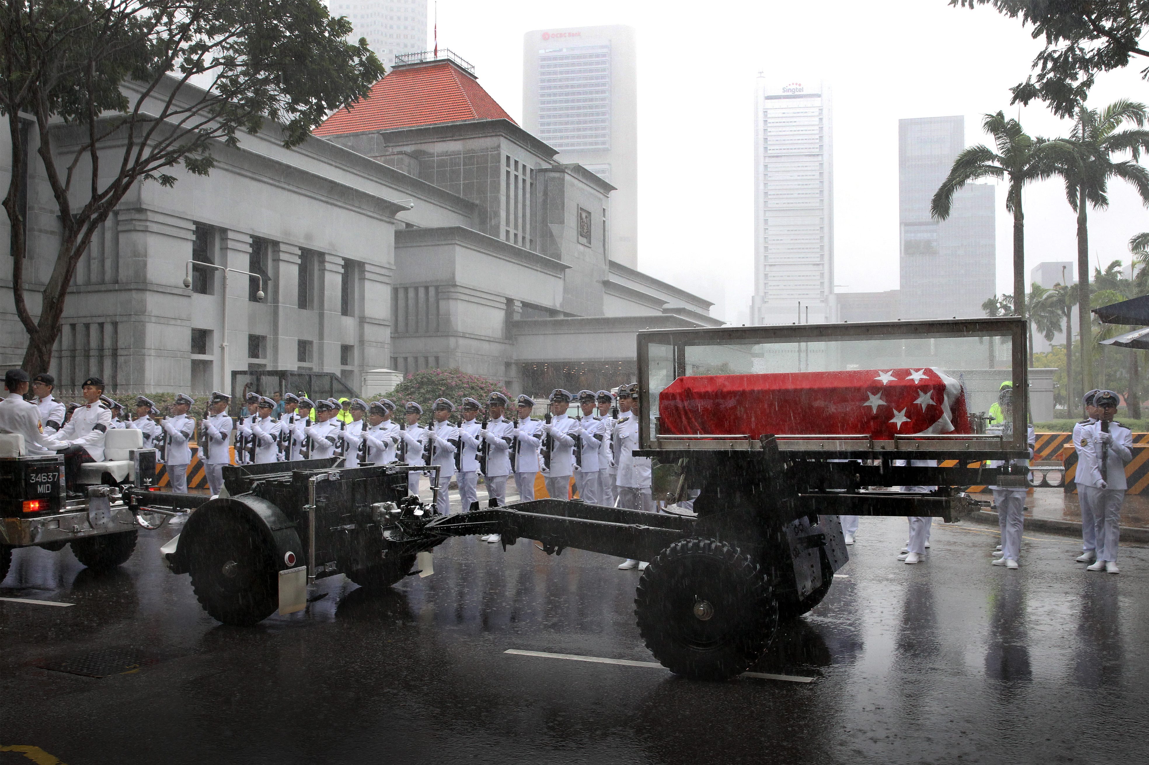 Singaporean state funeral in rain: Casket with flag on gun carriage, honor guard in white uniforms.