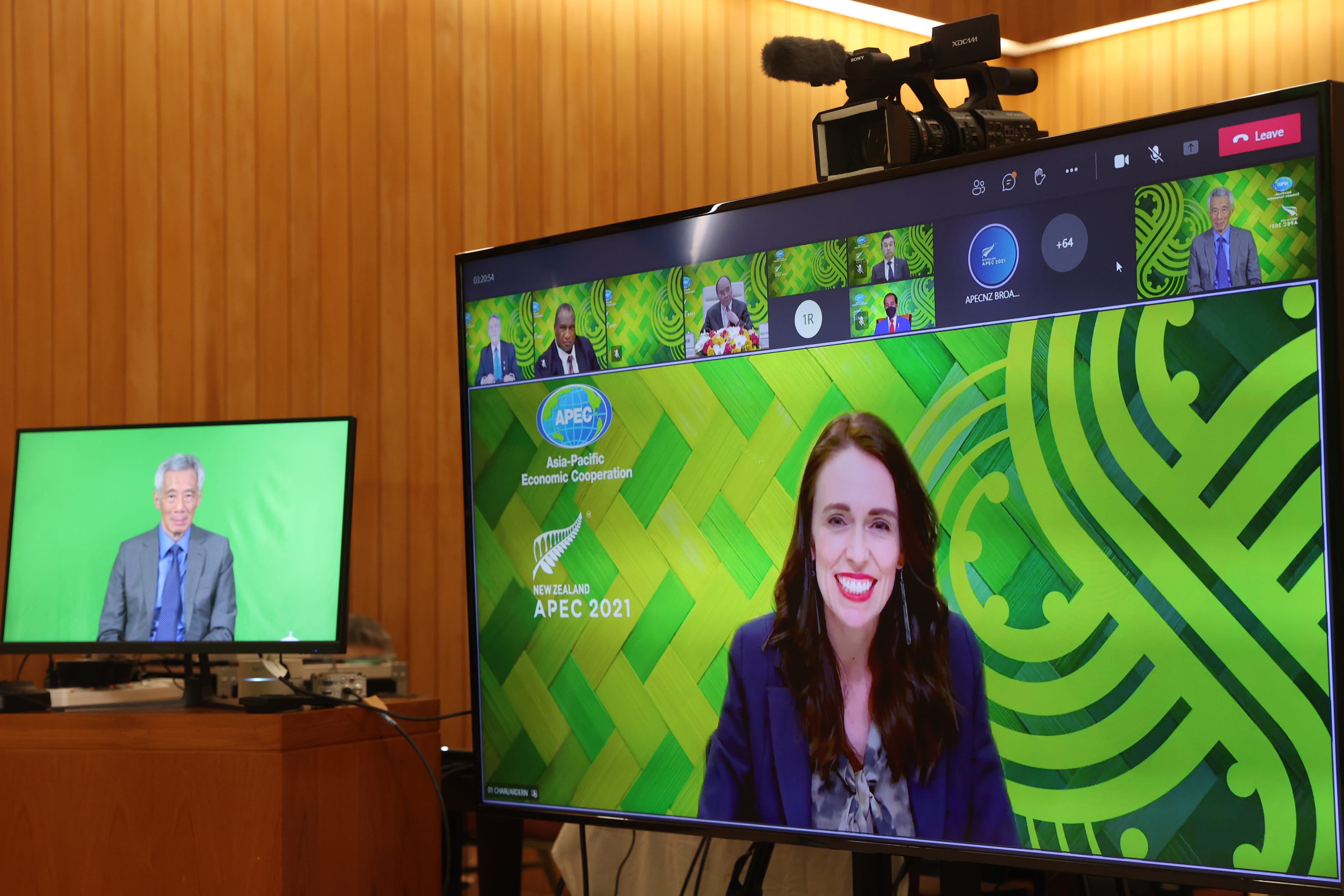 Jacinda Ardern on large video call screen; APEC 2021 logo. Monitor shows other participants. Sony camera on top.