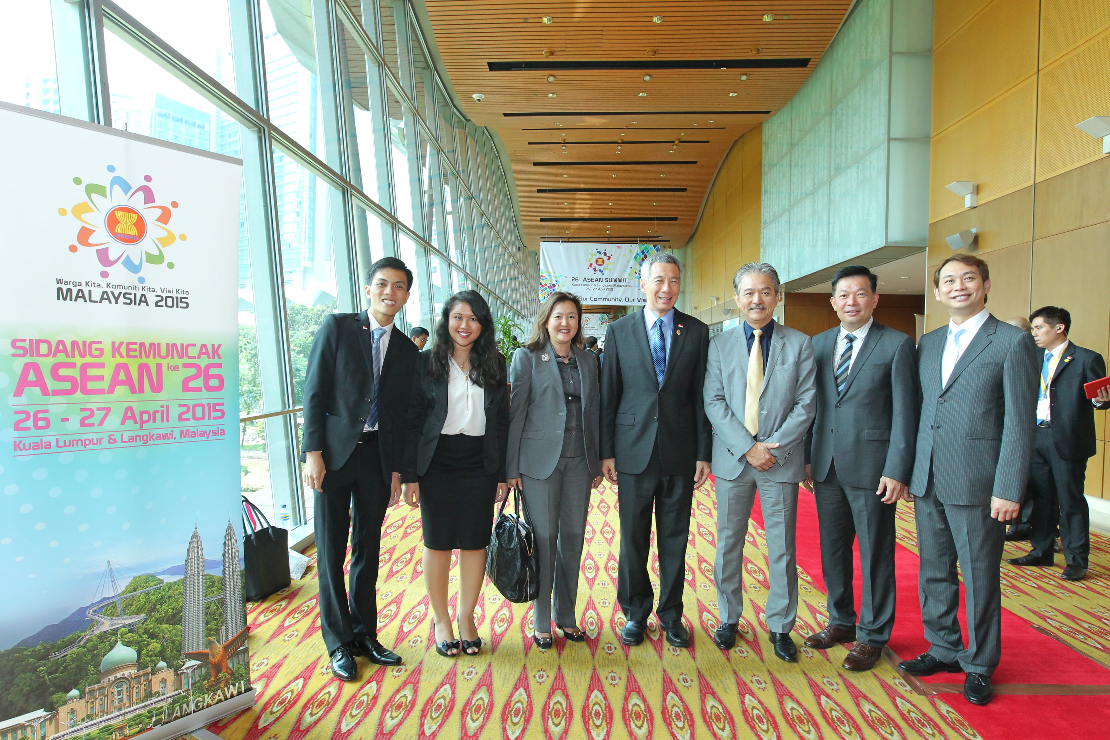 Group of people in suits posing in front of an ASEAN summit banner.