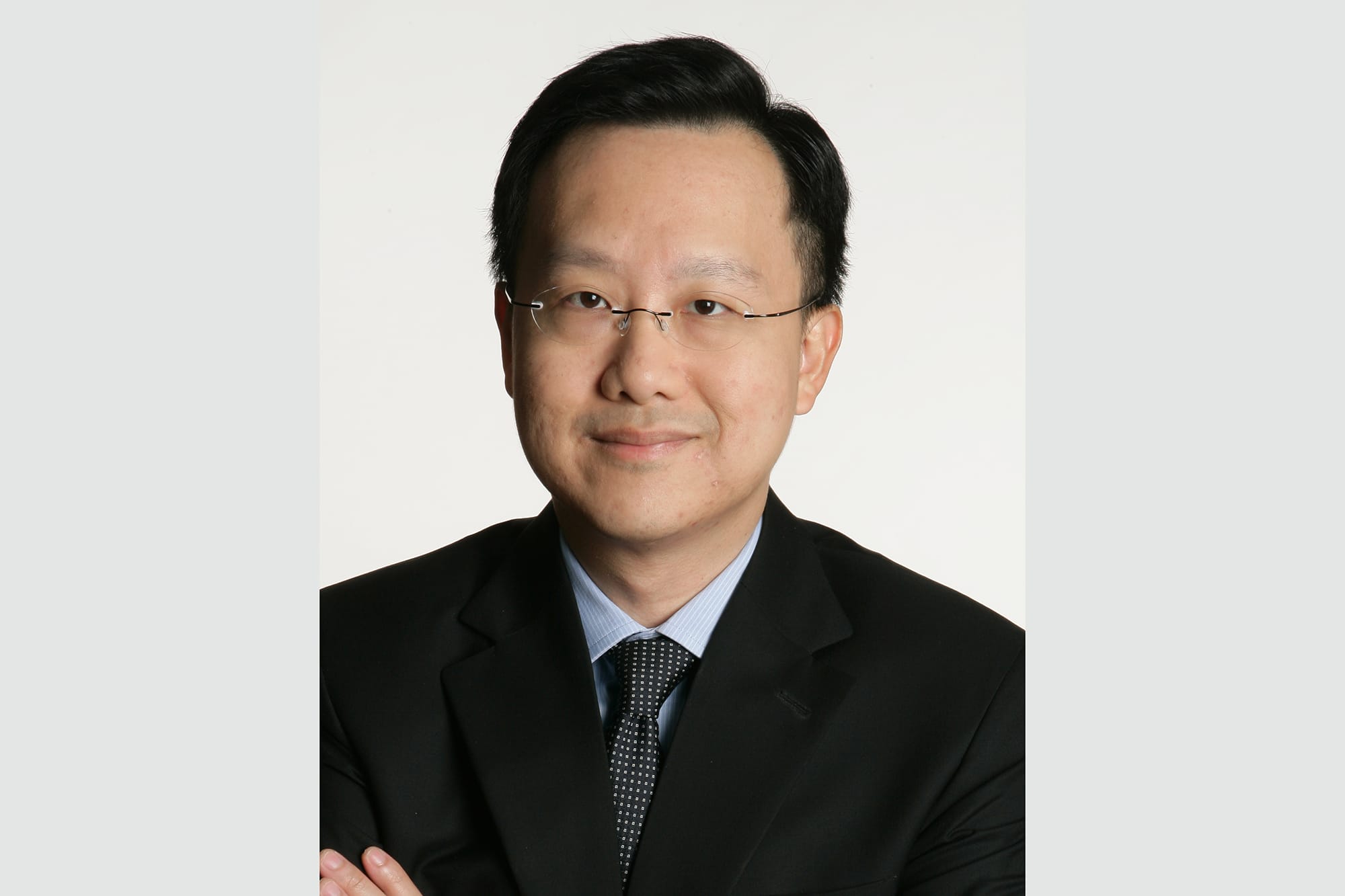 Headshot of a person with glasses, wearing a black suit and tie on white background.