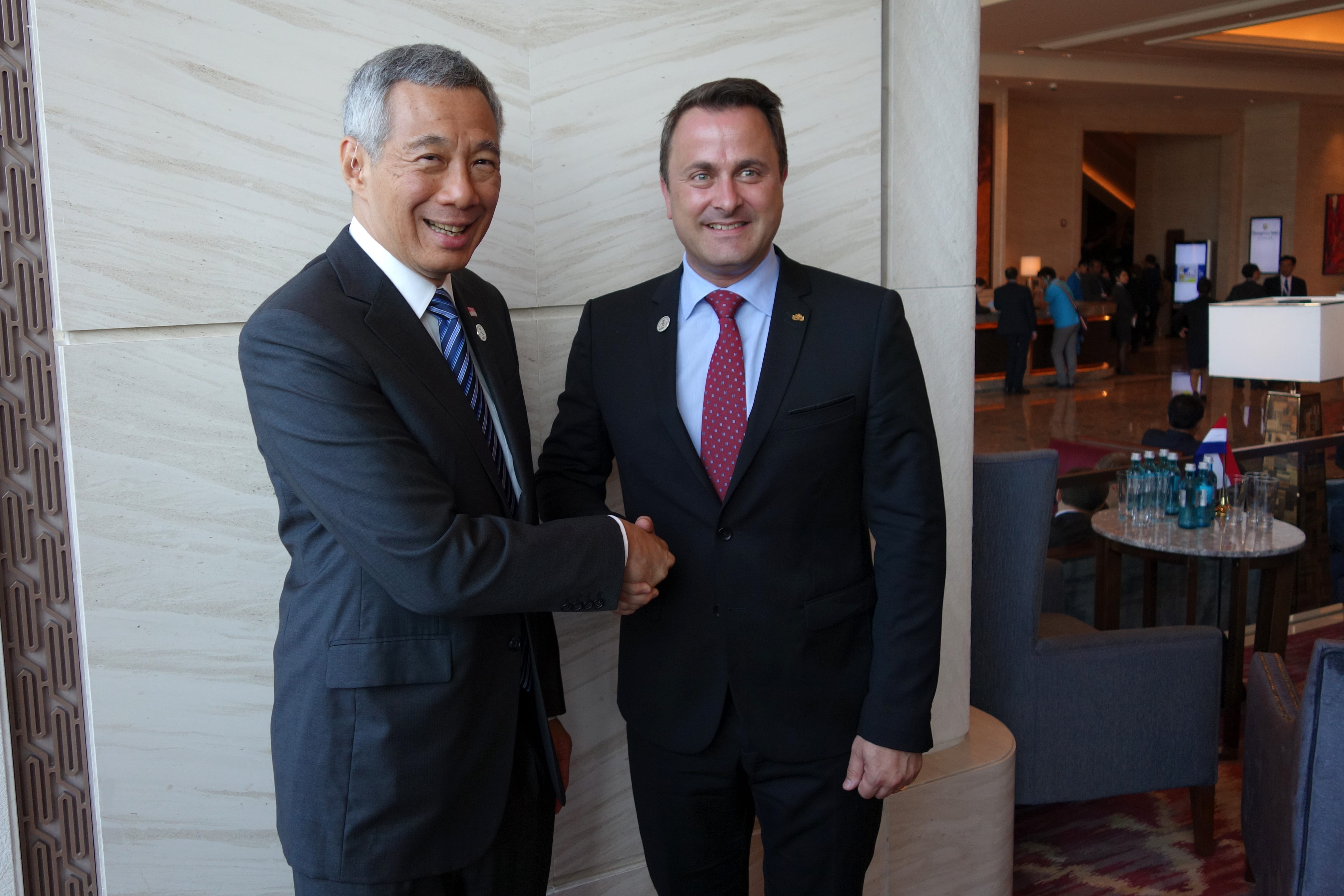 Lee Hsien Loong and Xavier Bettel in suits shake hands indoors.
