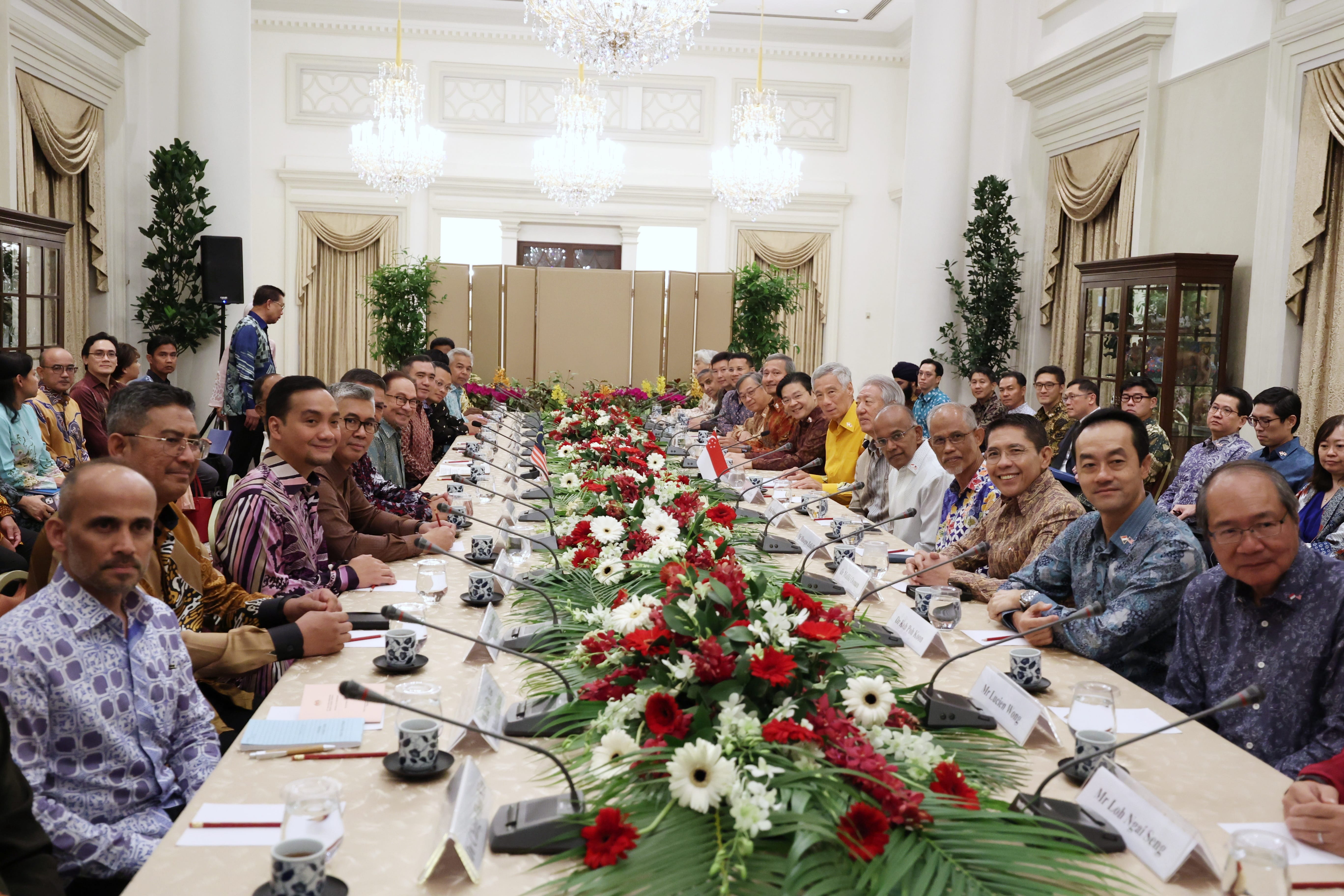 Group of people at a long table with floral arrangements and microphones.