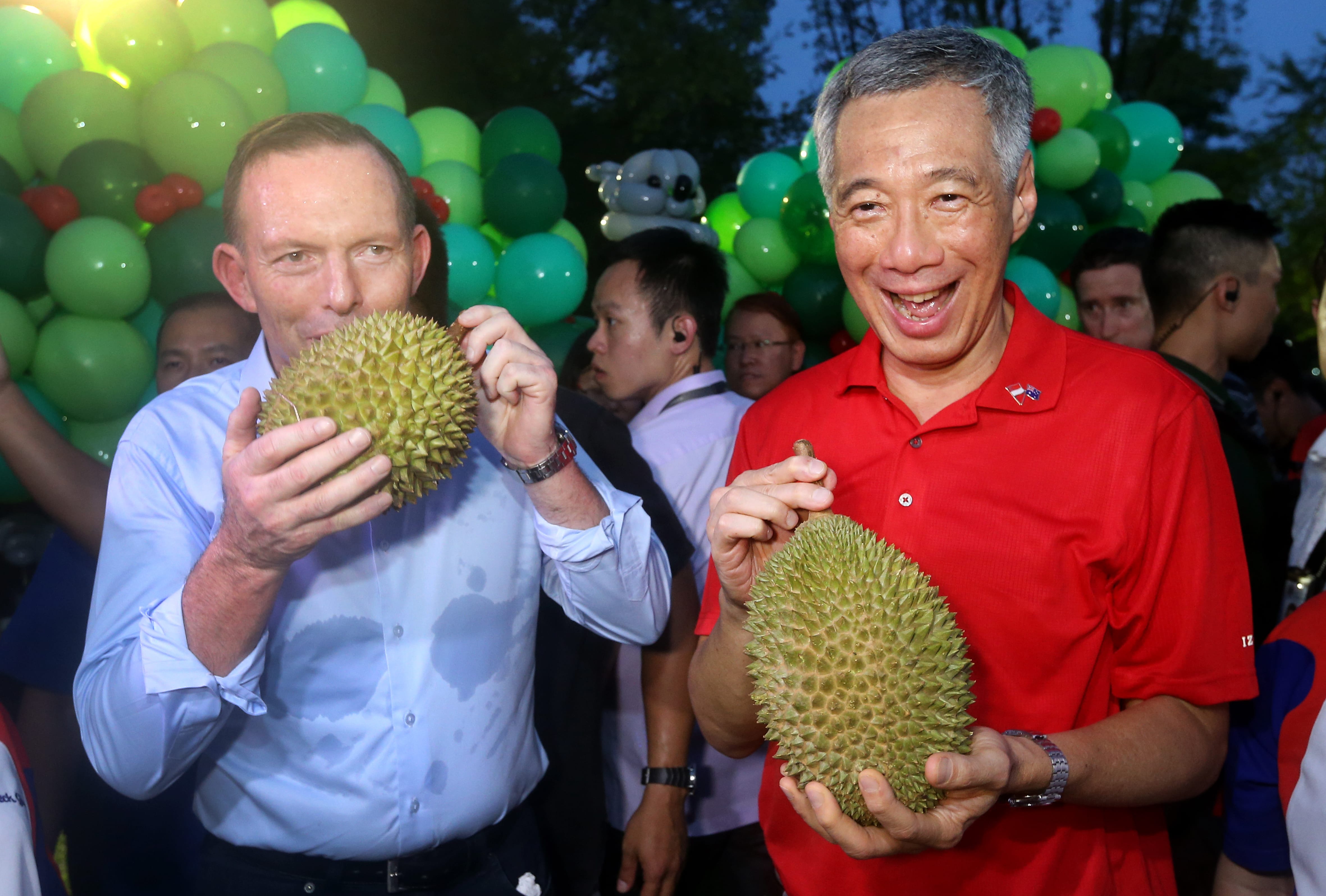 Tony Abbott and Lee Hsien Loong hold spiky durian fruit amid green balloons.