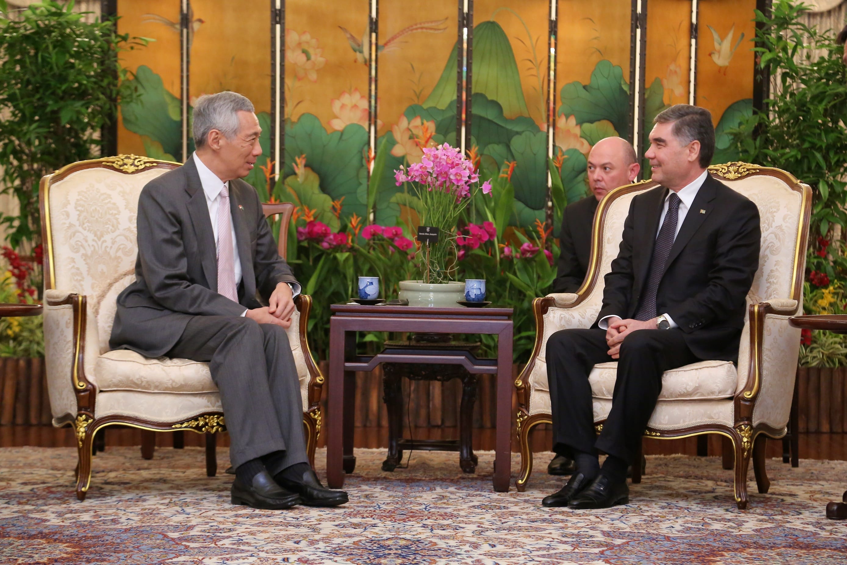 Lee Hsien Loong and Gurbanguly Berdimuhamedow sit in ornate chairs on a patterned rug. Floral screen behind.