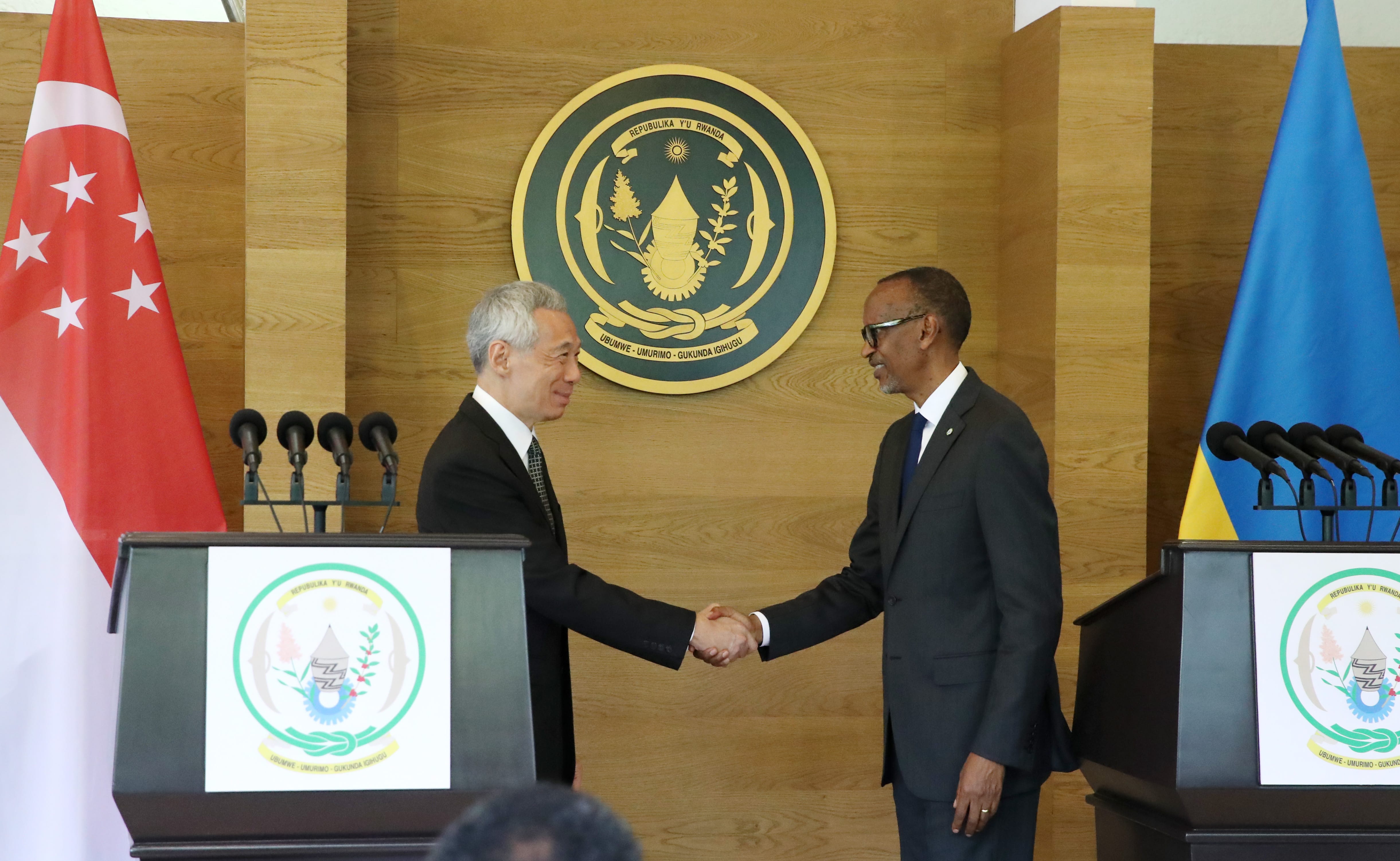 Lee Hsien Loong and Paul Kagame shake hands with Rwanda and Singapore flags behind them.