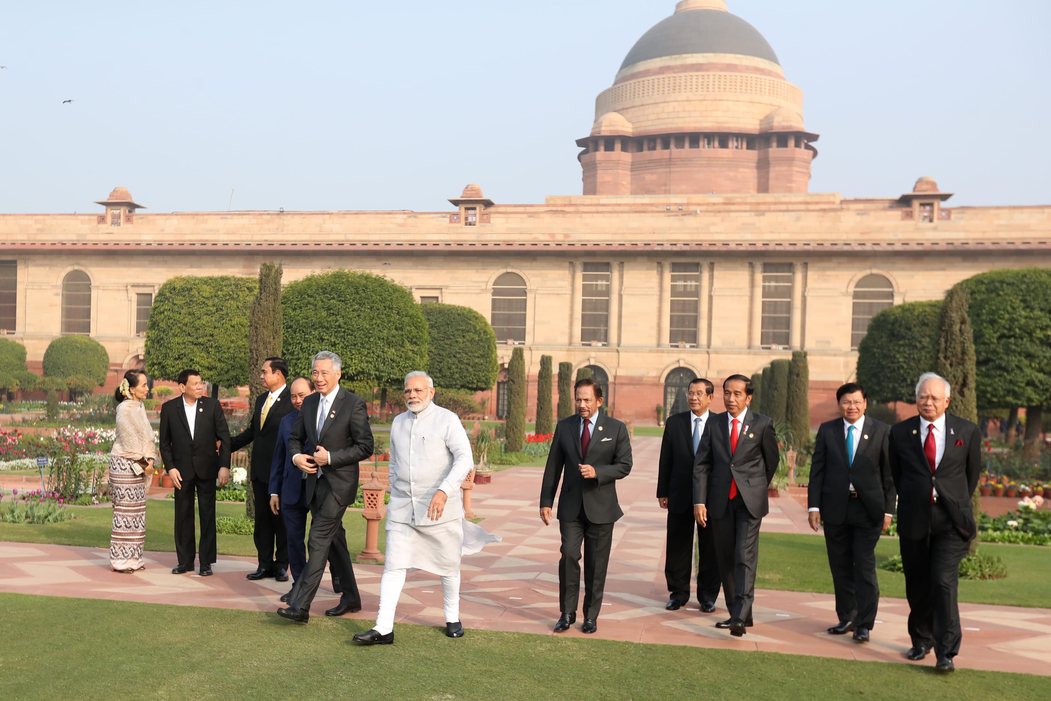 Group of world leaders walking in a garden with Rashtrapati Bhavan in background.