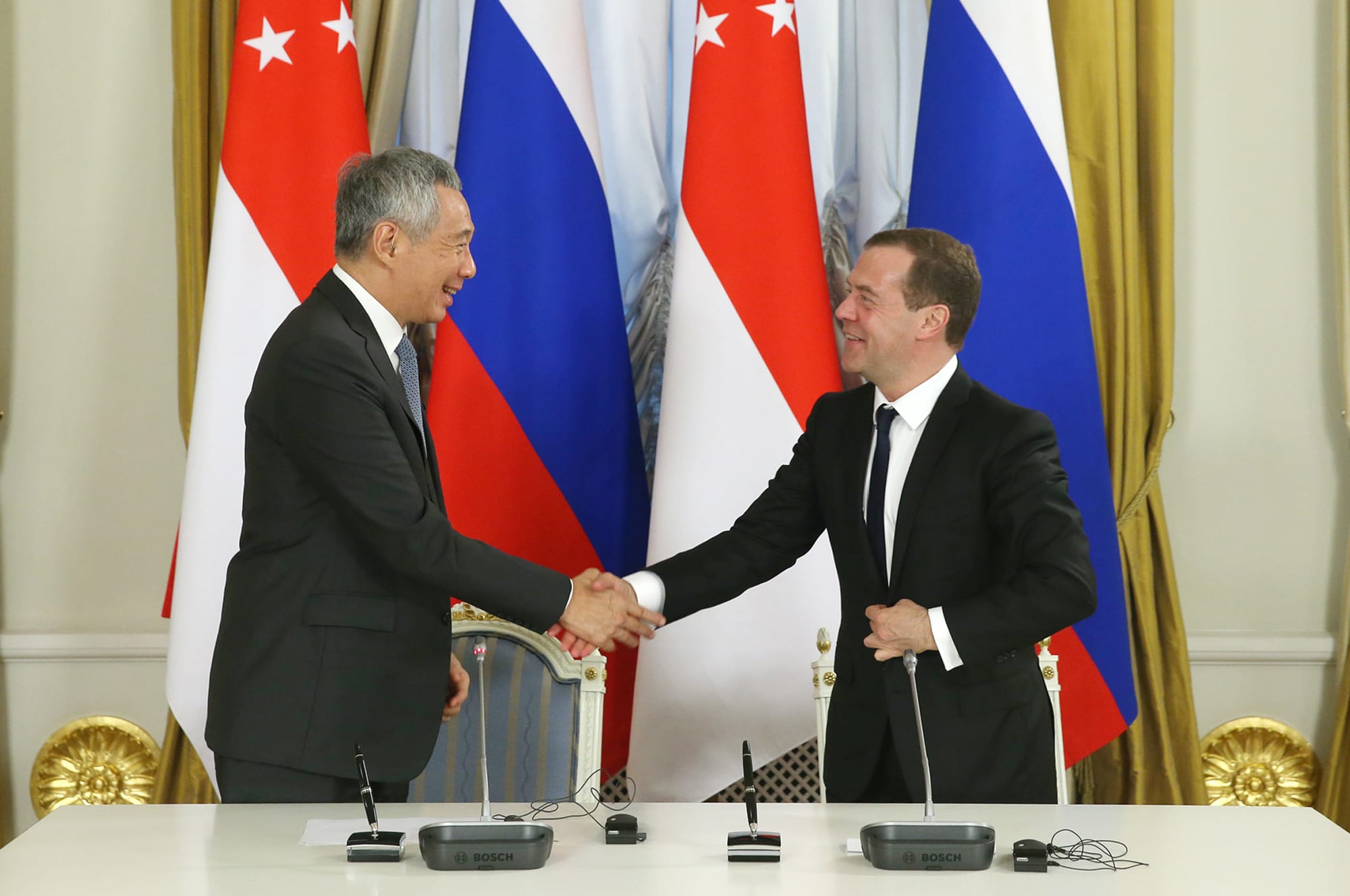 Two men in suits shake hands, Singapore and Russia flags behind them. Bosch mics on table.