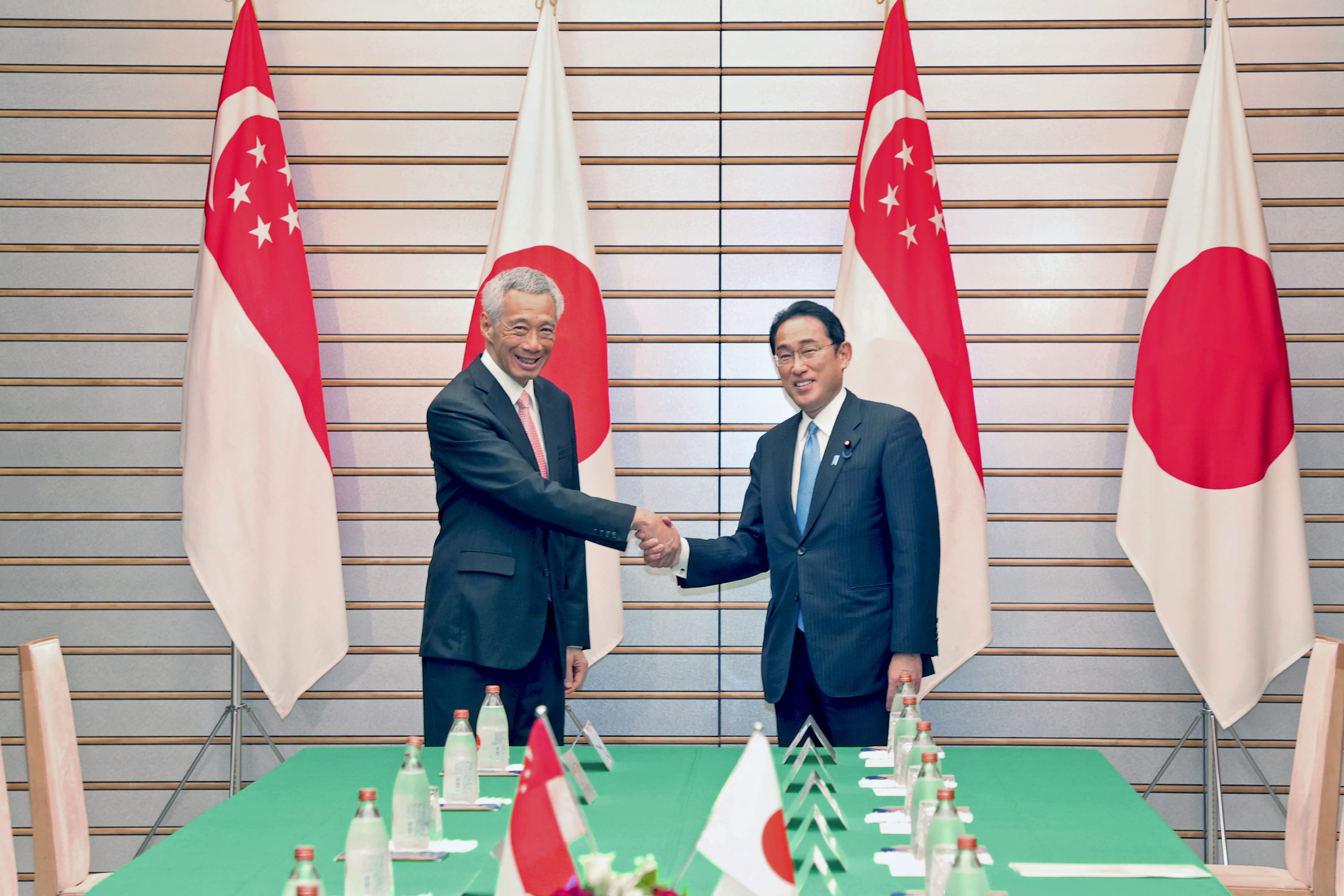 Lee Hsien Loong and Fumio Kishida shaking hands before Singapore and Japan flags.