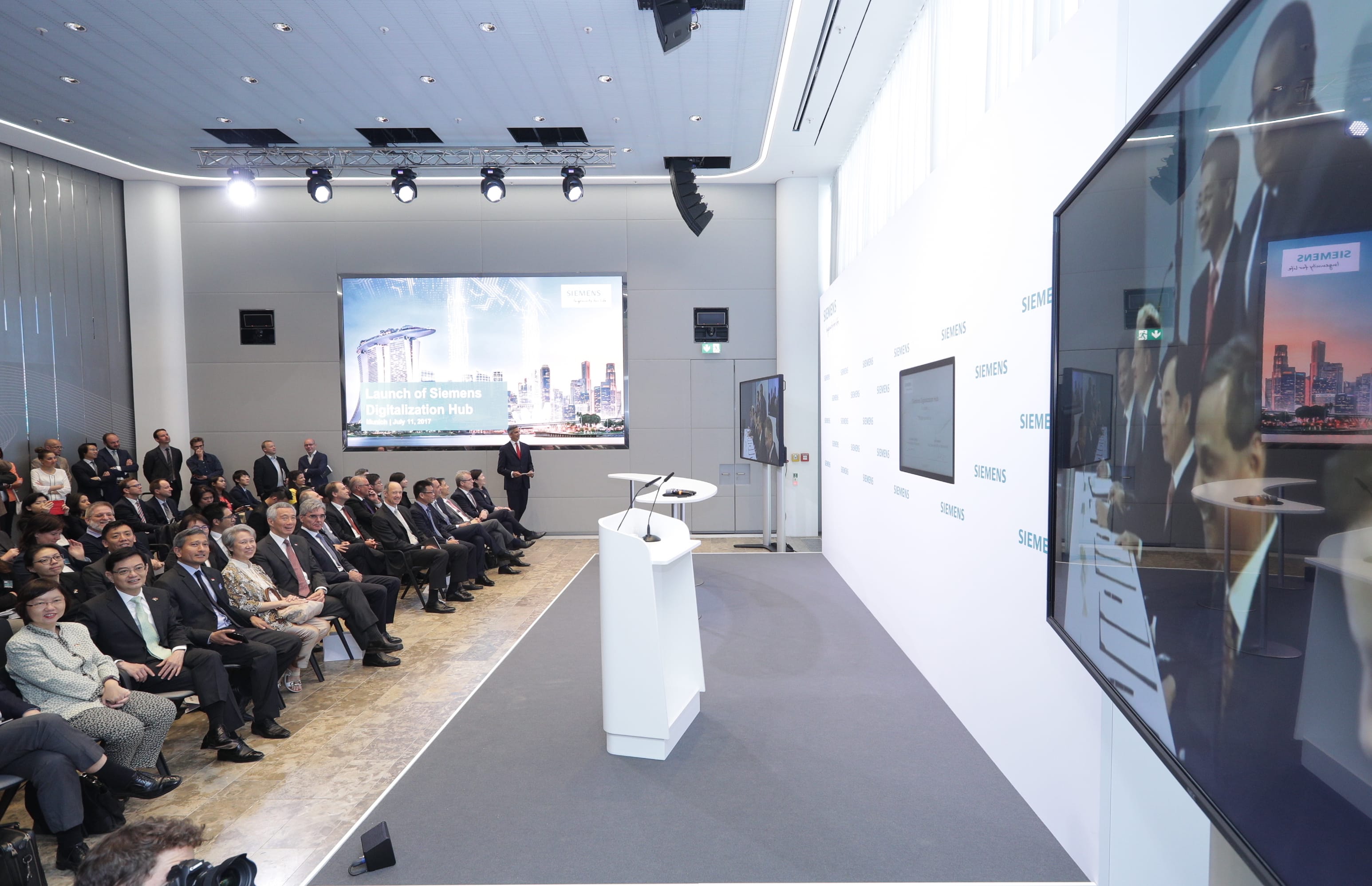 Audience at Siemens event. Presenter near podium, large screen displays Singapore skyline.