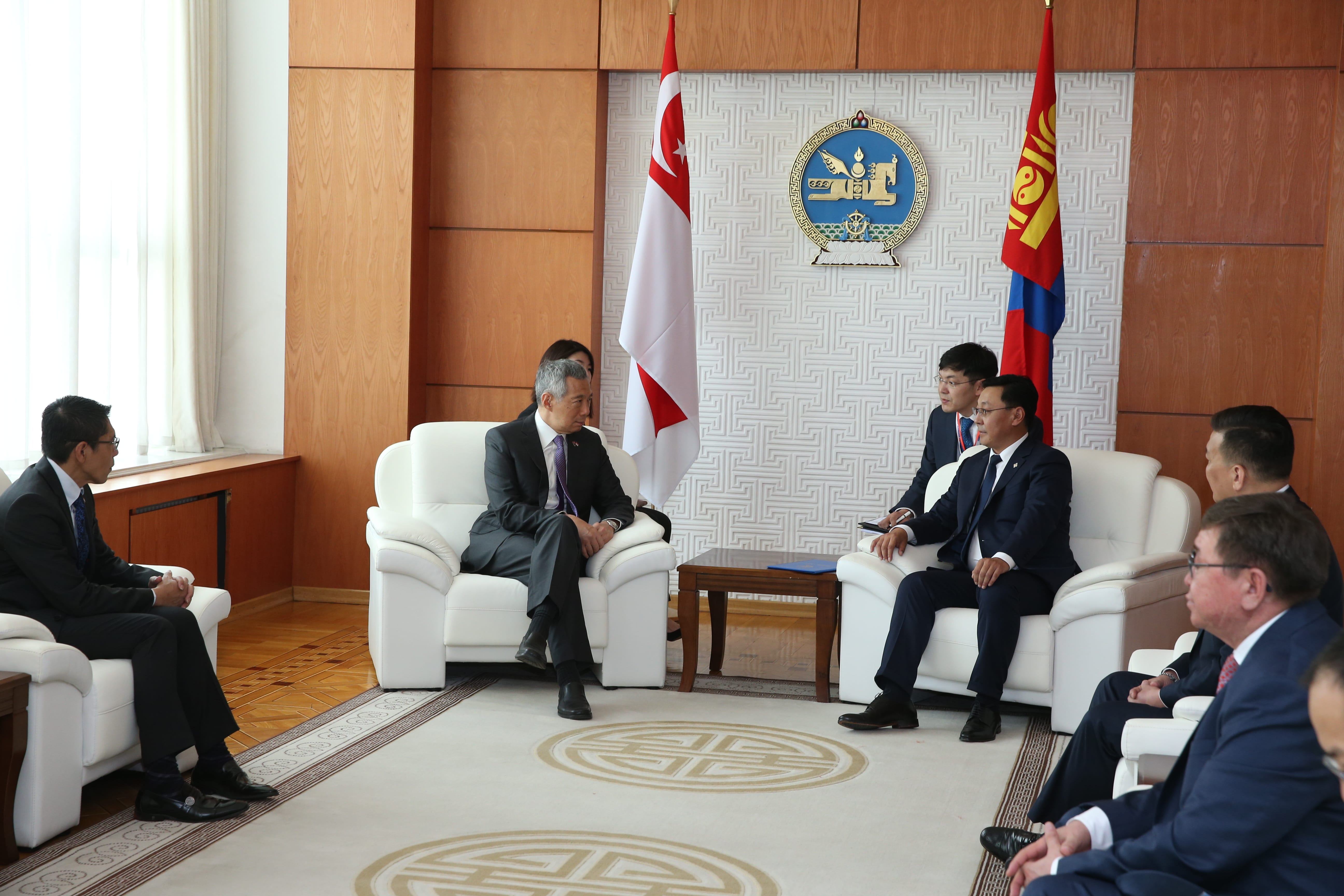 People in suits seated in a room with Singaporean and Mongolian flags.