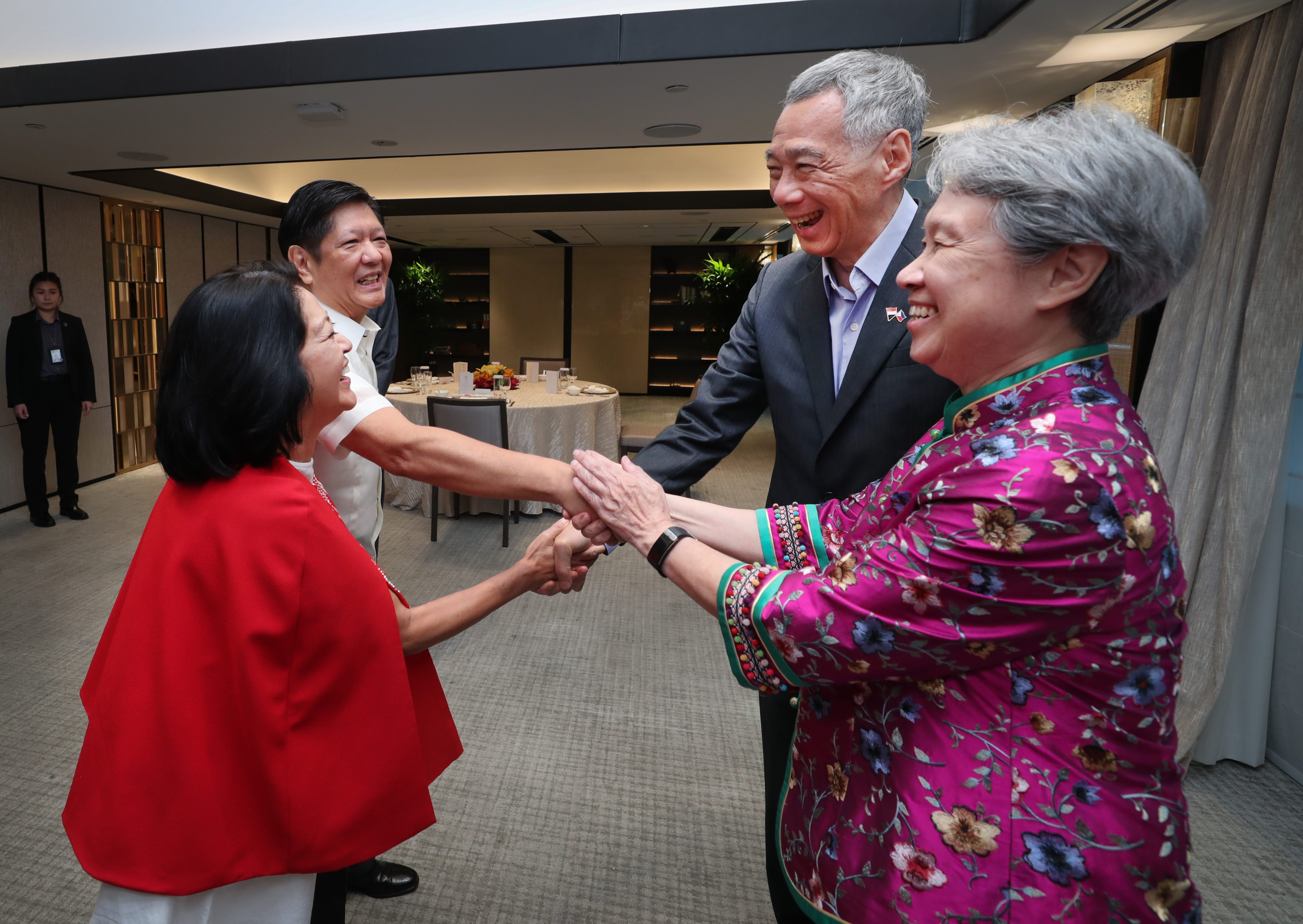 Lee Hsien Loong and Marcos families smiling and shaking hands indoors.
