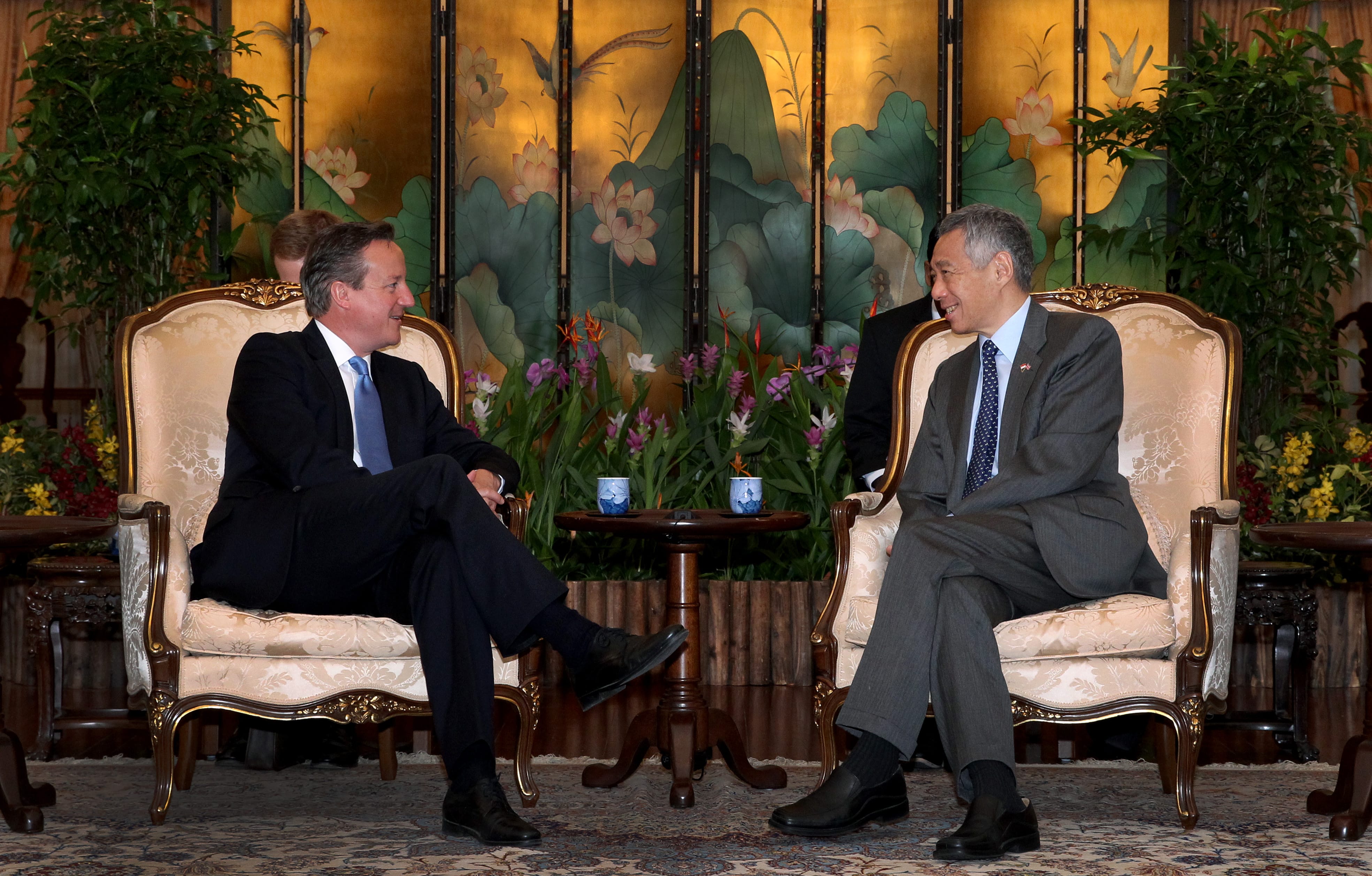 Two men in suits, David Cameron and Lee Hsien Loong, sit in ornate chairs facing each other.