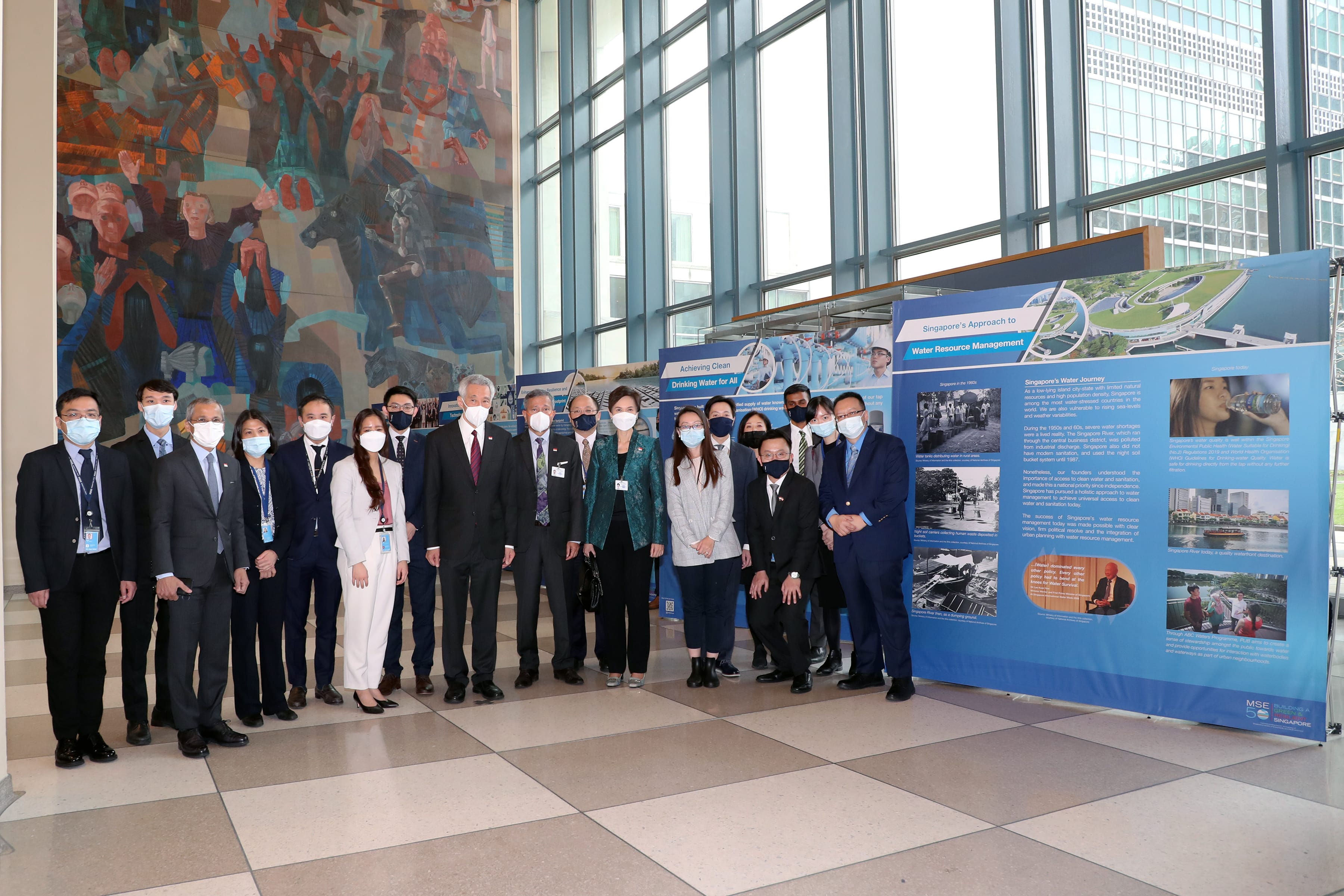 Group of people posed in front of exhibit on Singapore's water management. Large mural and windows in background.