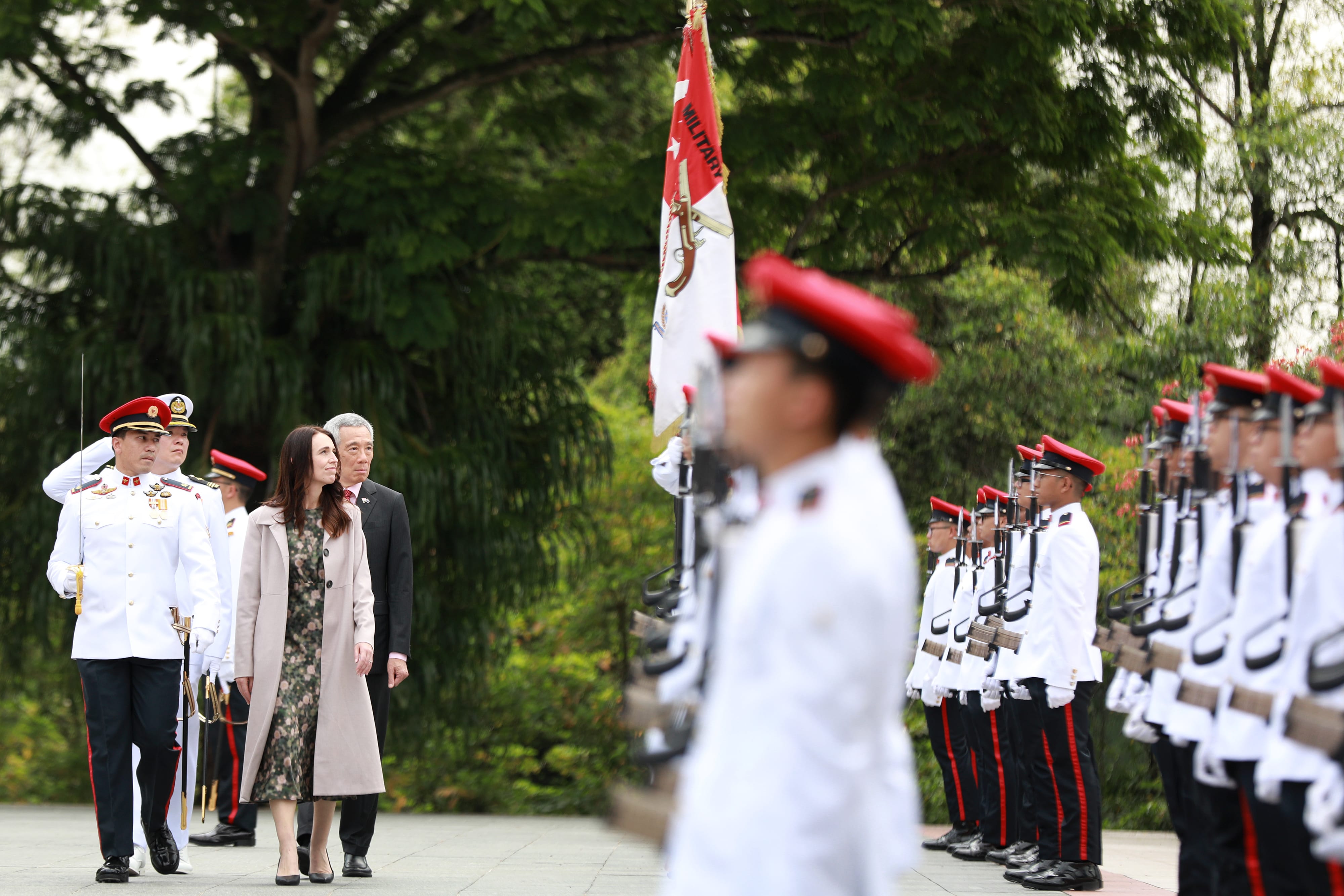Jacinda Ardern and Lee Hsien Loong inspect a military honor guard outdoors.