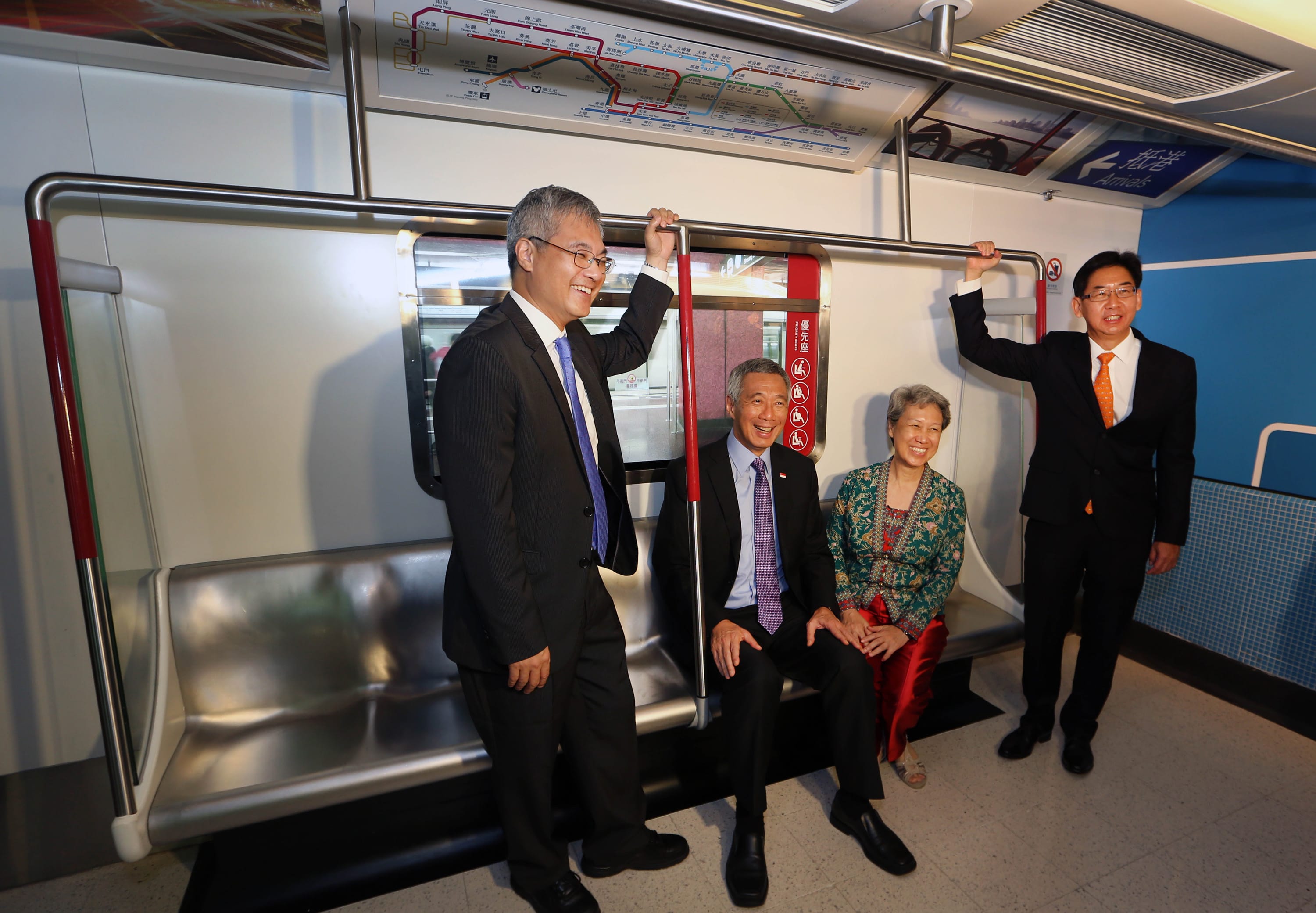 Four people inside a subway car with route map and stainless steel handrails overhead.