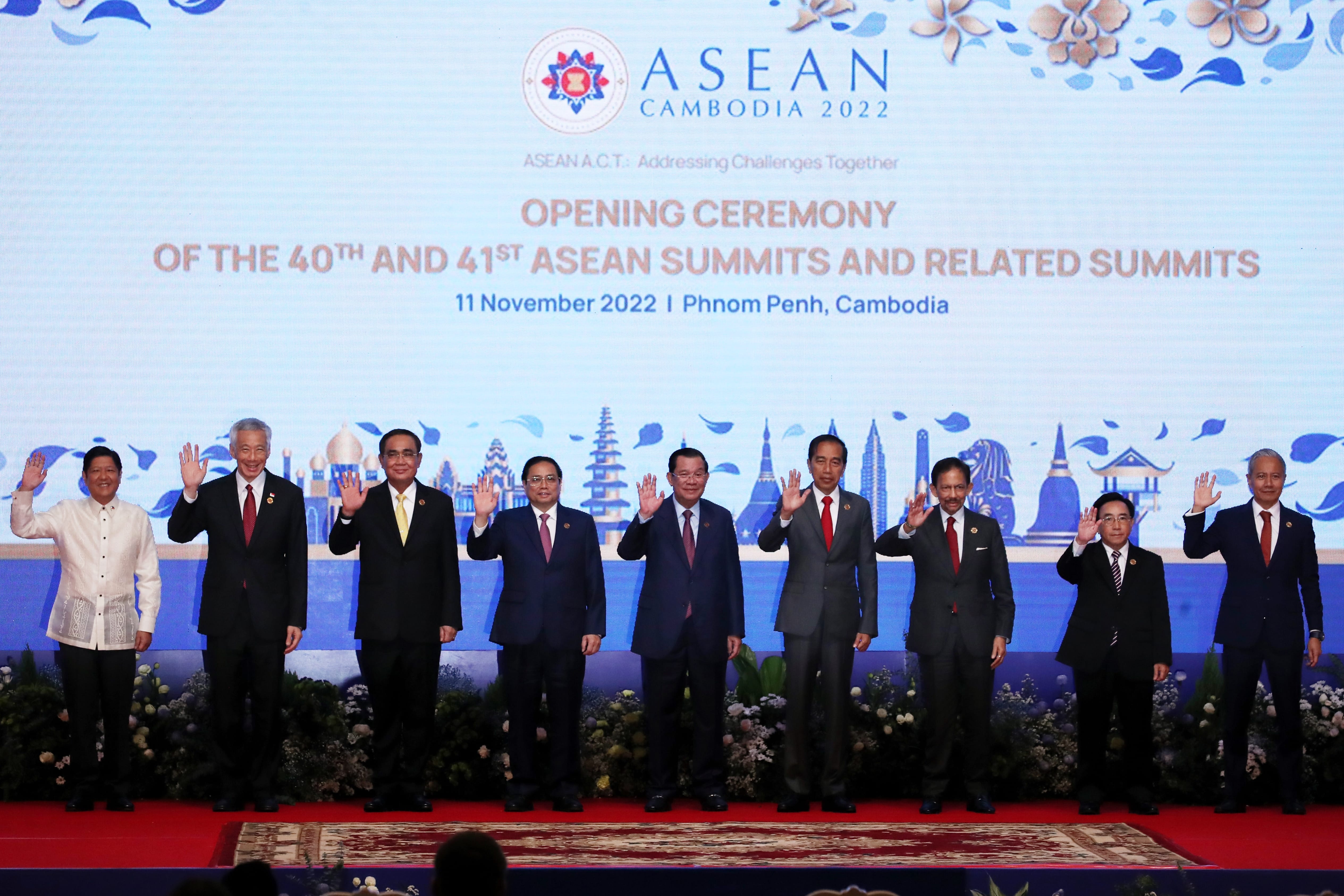 Nine people in suits wave in front of "ASEAN CAMBODIA 2022" backdrop.